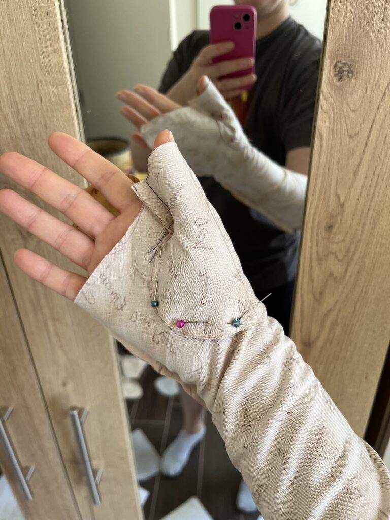 A hand wearing a mockup for 18th century linen mitts faces the camera palm-up