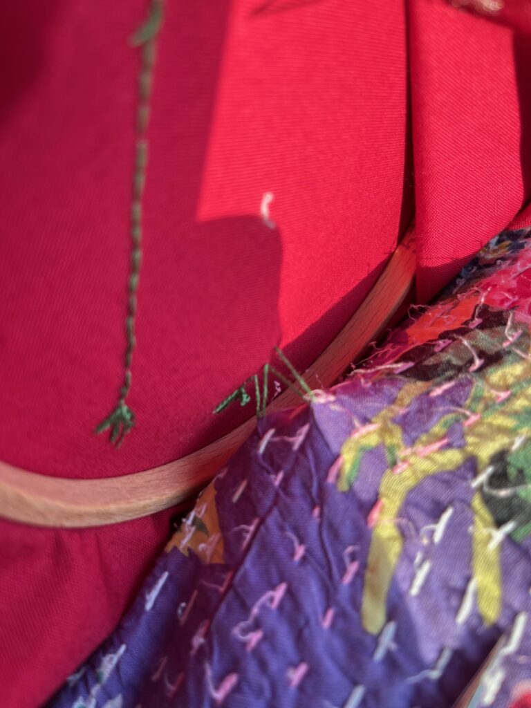Red fabric in an embroidery frame is accidentally stitched to a purple cushion.