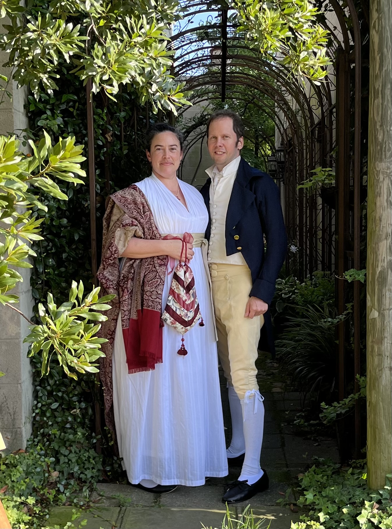 A man and woman dressed in Regency clothing stand together facing the camera.