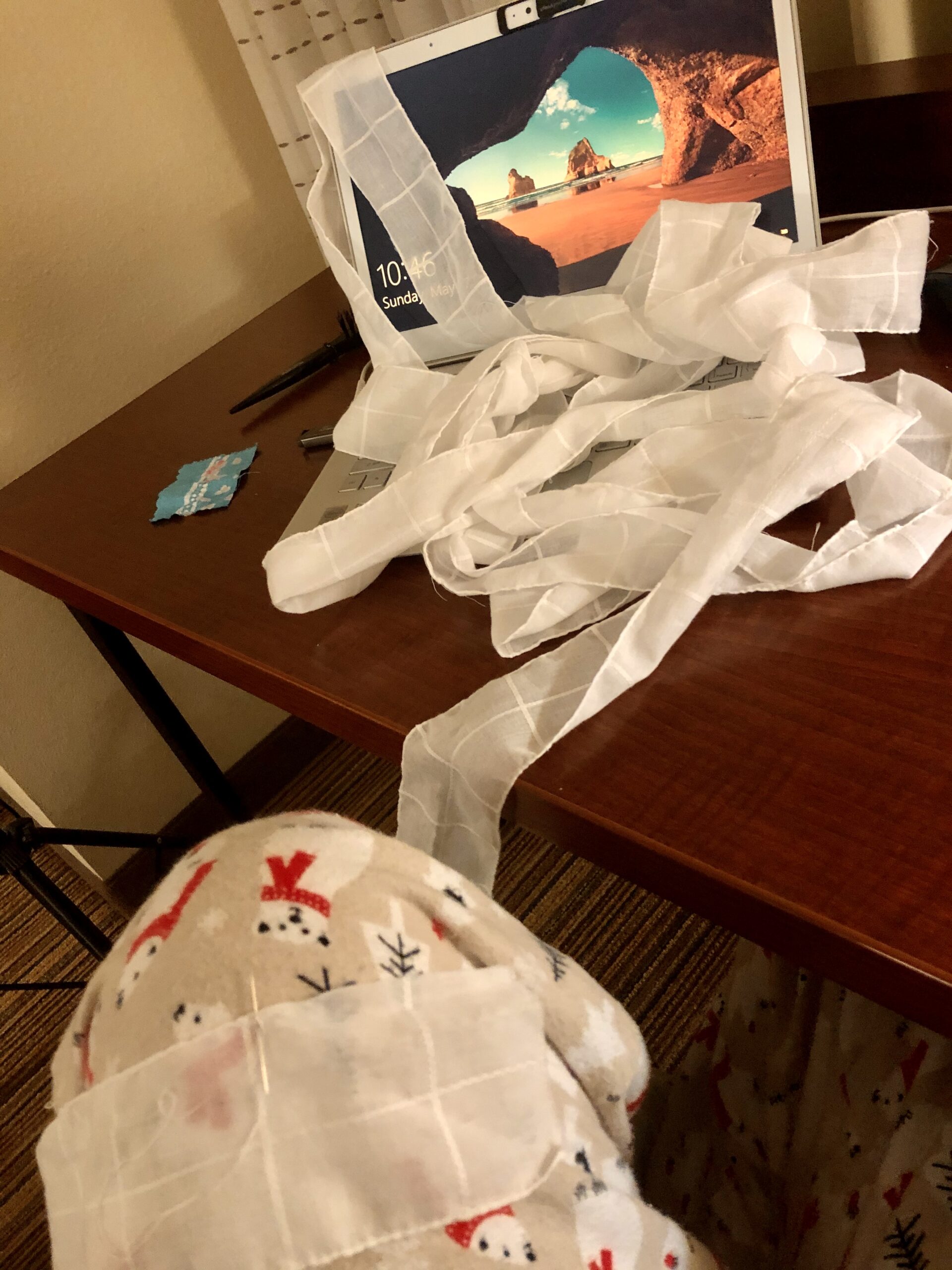 A long white cotton band lies piled on a wooden desk. At the front of the image, the strip is draped over a knee clad in flannel PJs.