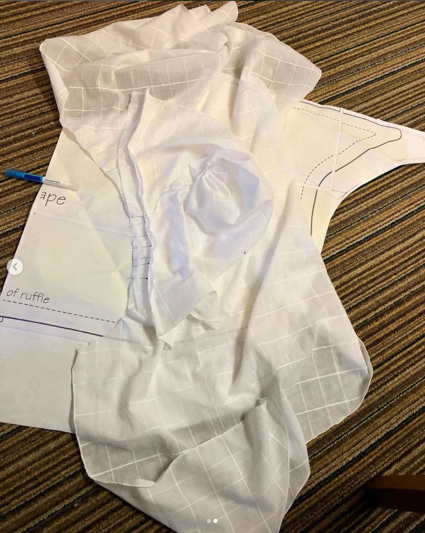 A pile of white cotton fabric lies on top of a paper pattern o a striped brown carpet