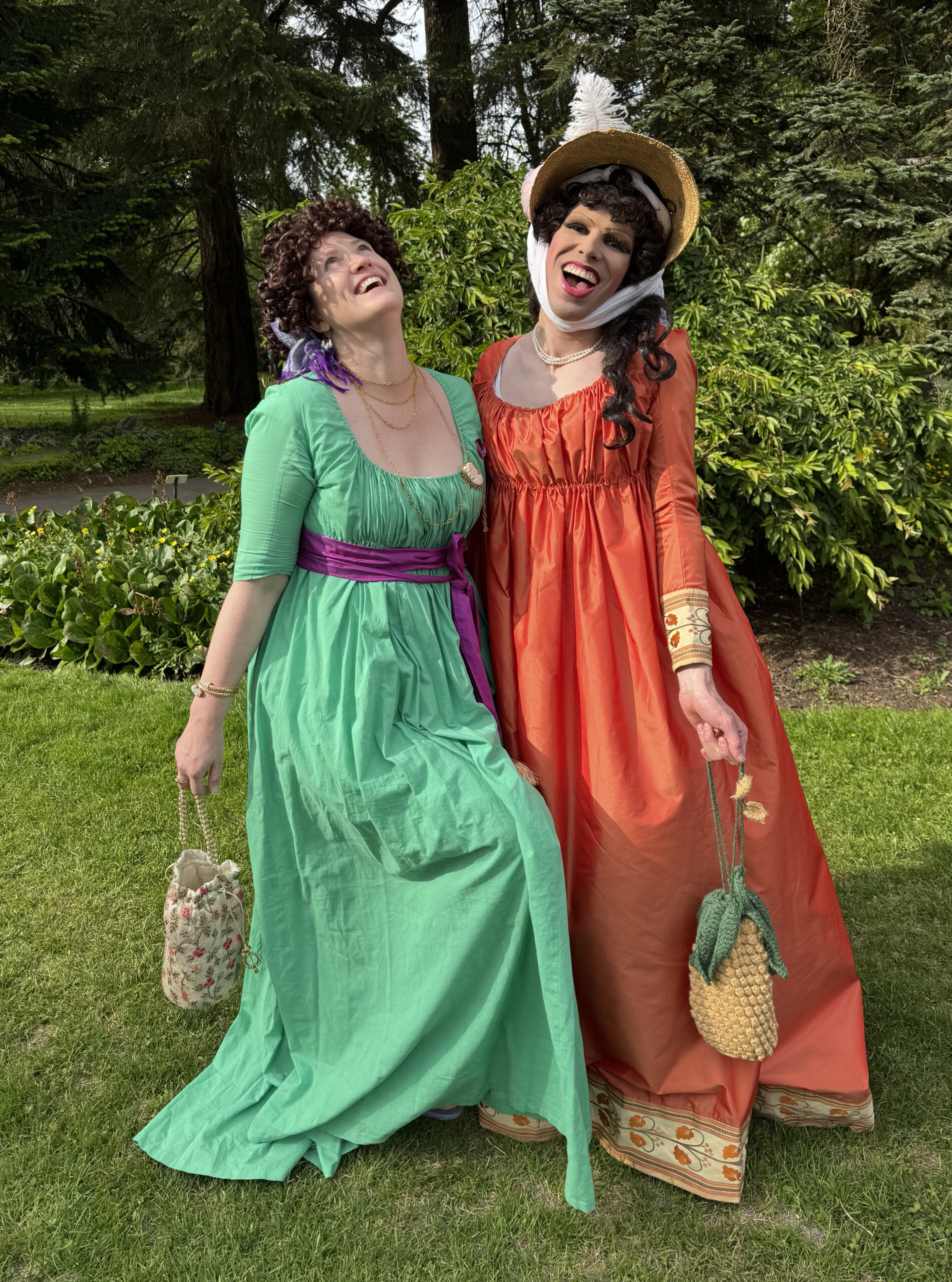two people dressed as regency merveilleuses laugh on a green lawn