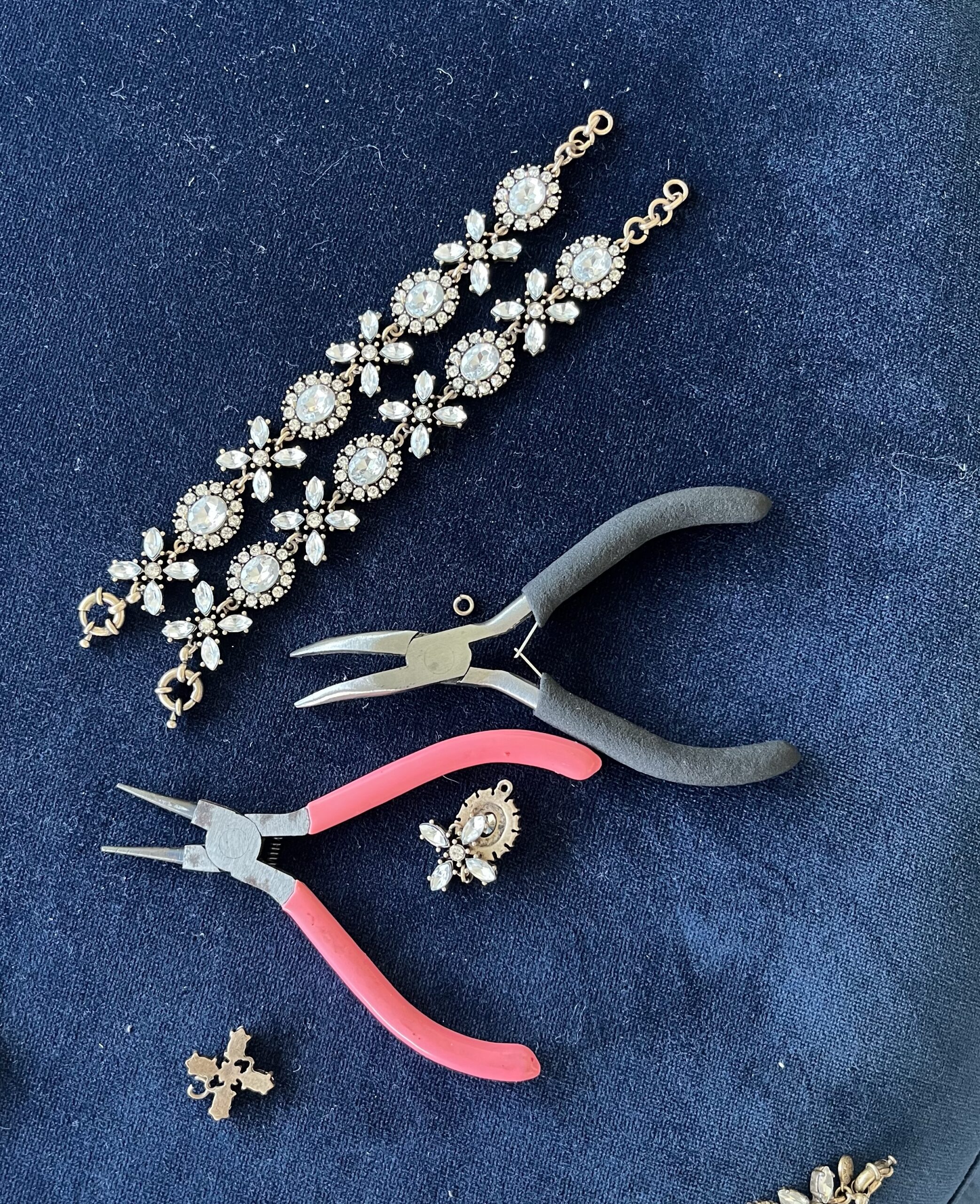 Two hug-and-kiss rhinestone bracelets lie on a bed of blue velvet beside two pairs of needle nose pliers