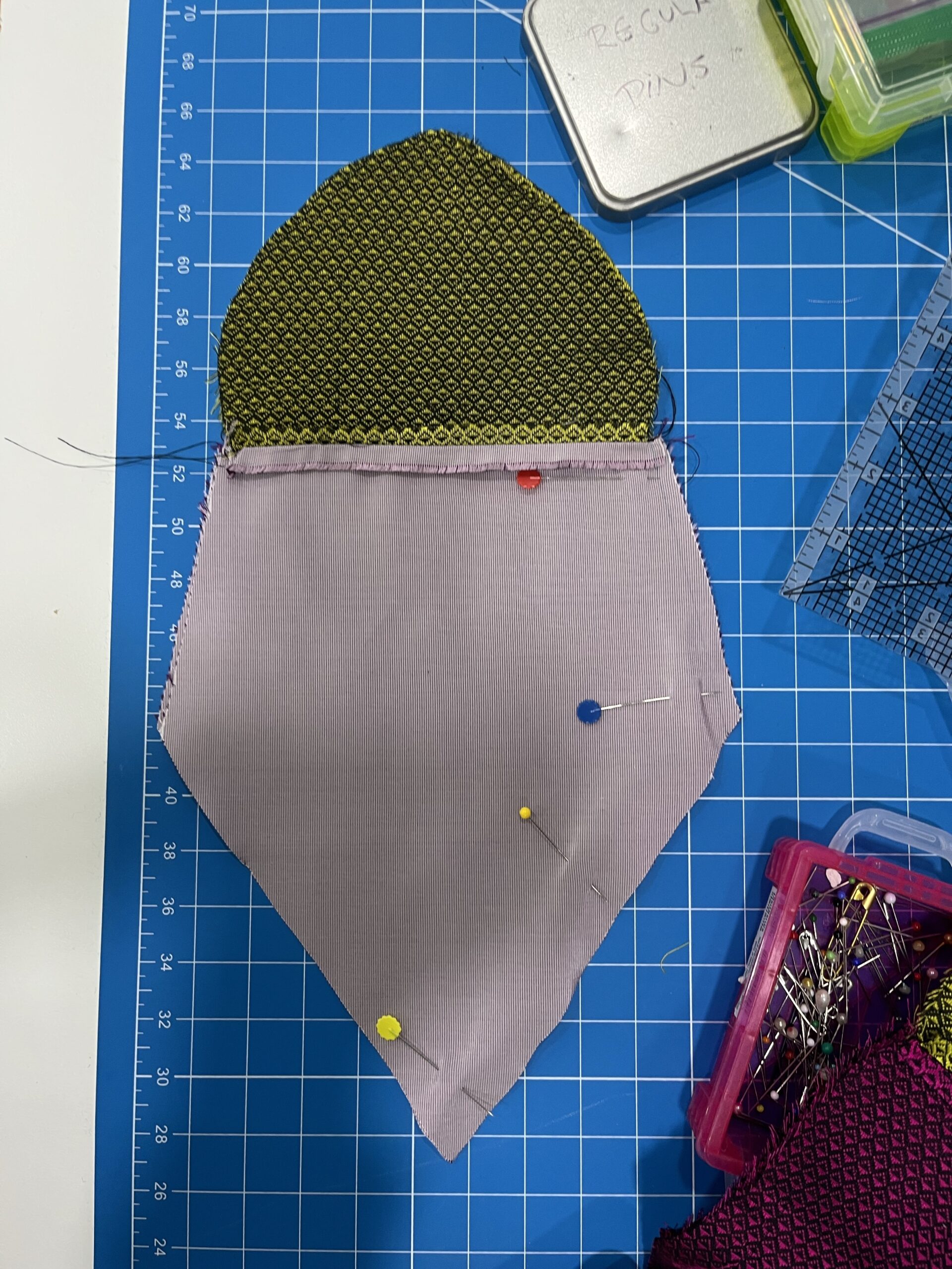 A pale lavender arrow-shaped piece of fabric lies on a cutting board. the top edge is stitched to a green petal shape in green silk