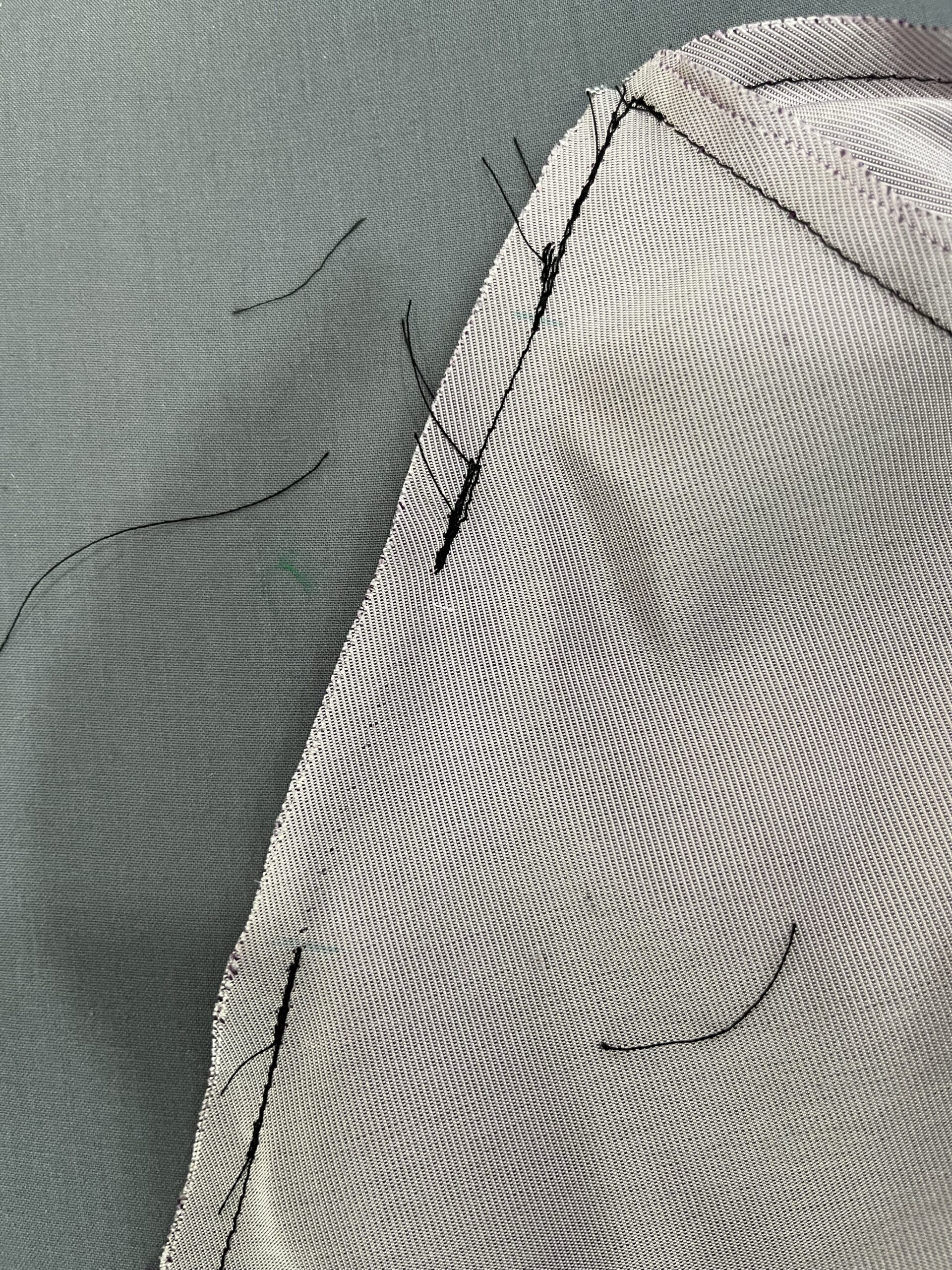 Close-up of a seam stitched in a piece of lavender silk. The seam is stitched with black thread. There is a 2 inch break in the seam