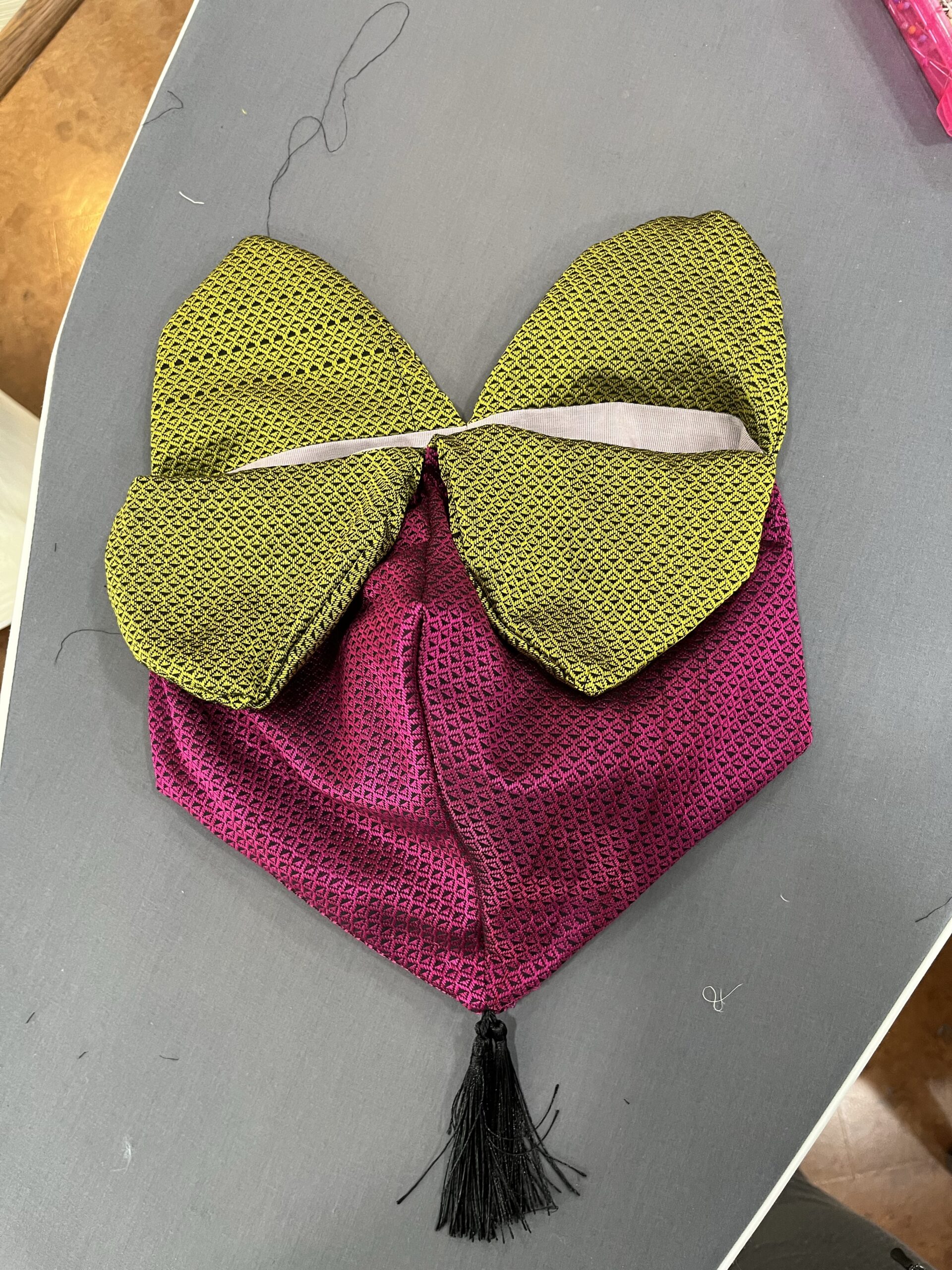 A raspberry regency reticule in pink and green silk lies on an ironing board. the seams are not yet pressed and it looks floppy and unformed
