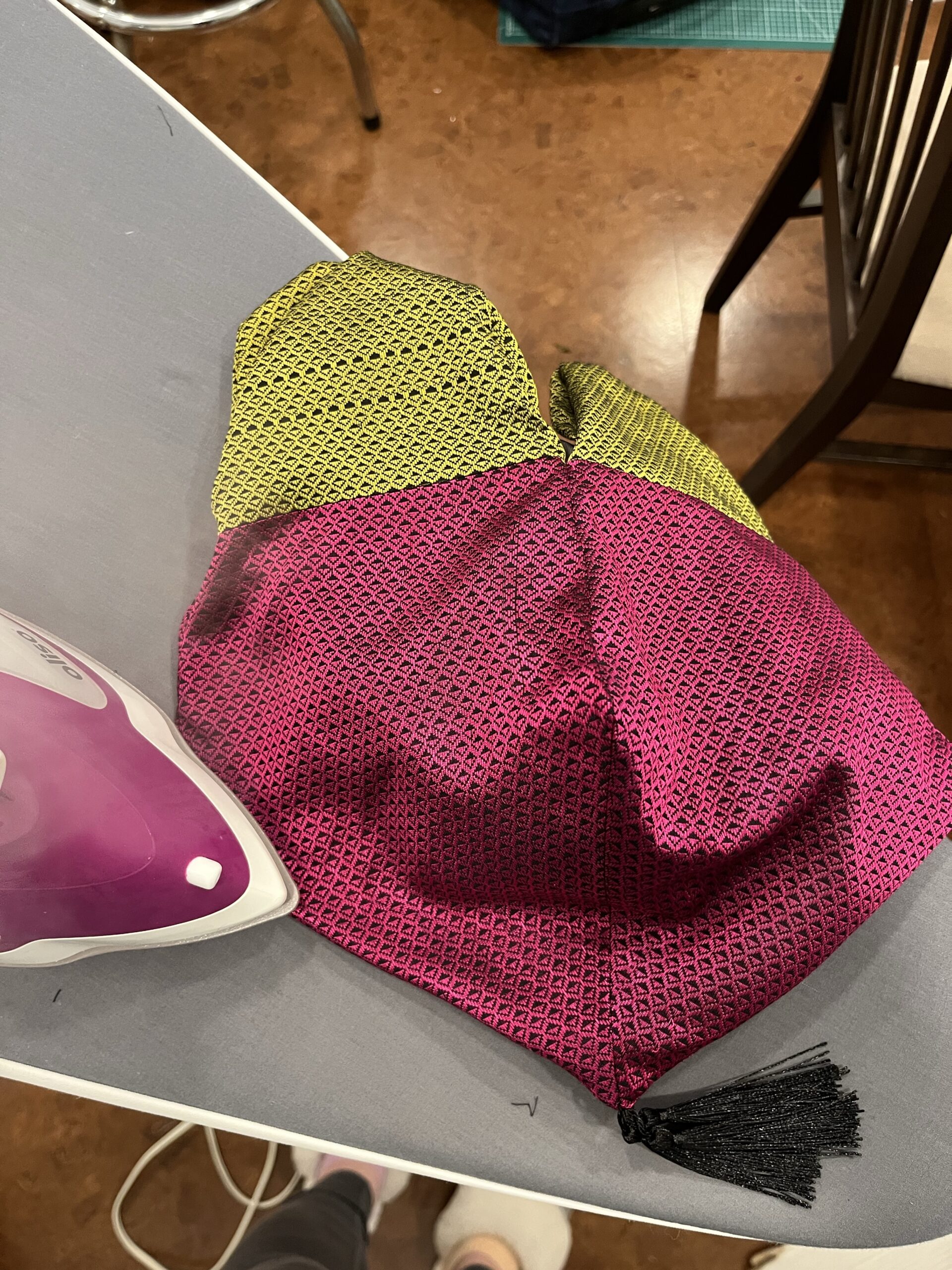 A regency reticule lies on a grey ironing board. A pink iron presses a seam on the reticule 