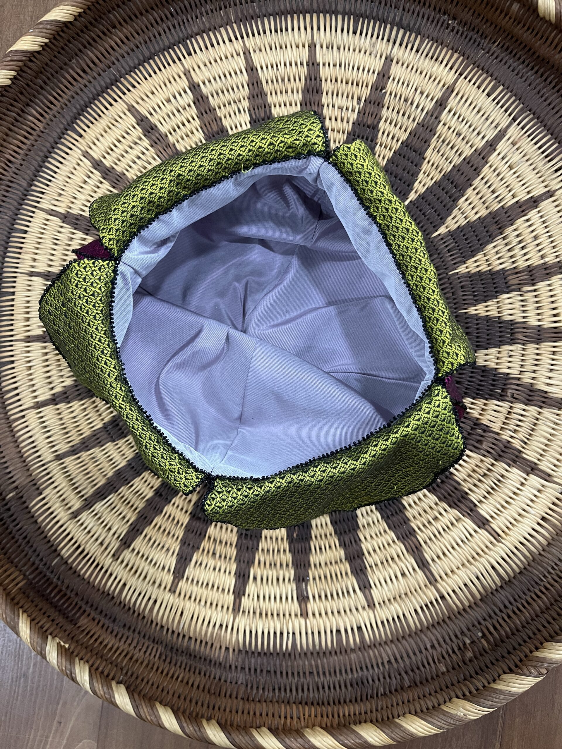 A regency reticule sits on a woven tray - the mouth of the reticule gapes open, edged by a trim of black seed beads