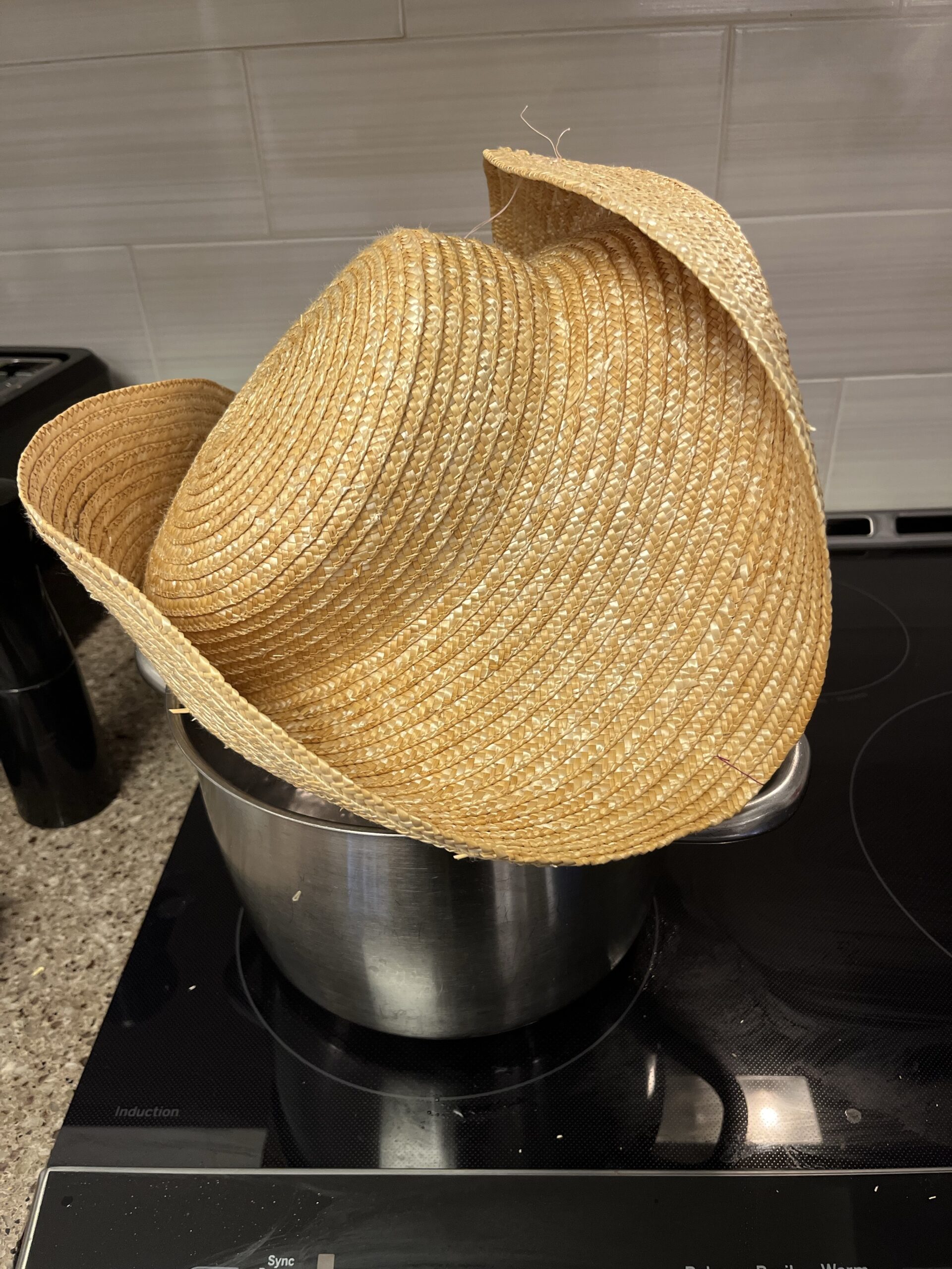 A large straw hat is being held over a pot of water on a stove top