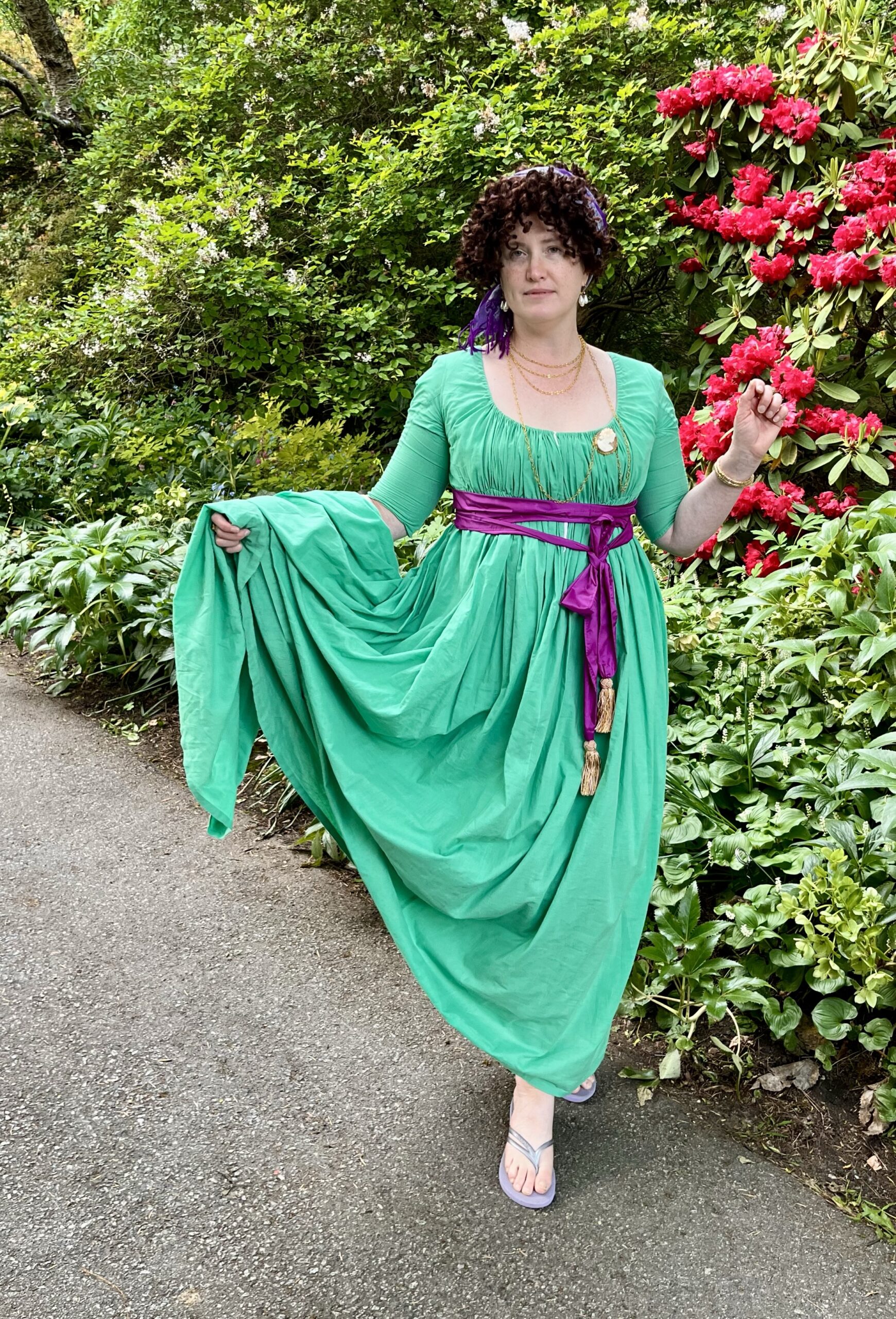 a woman dressed as a high fashion french merveilleuse stands on a gravel path
