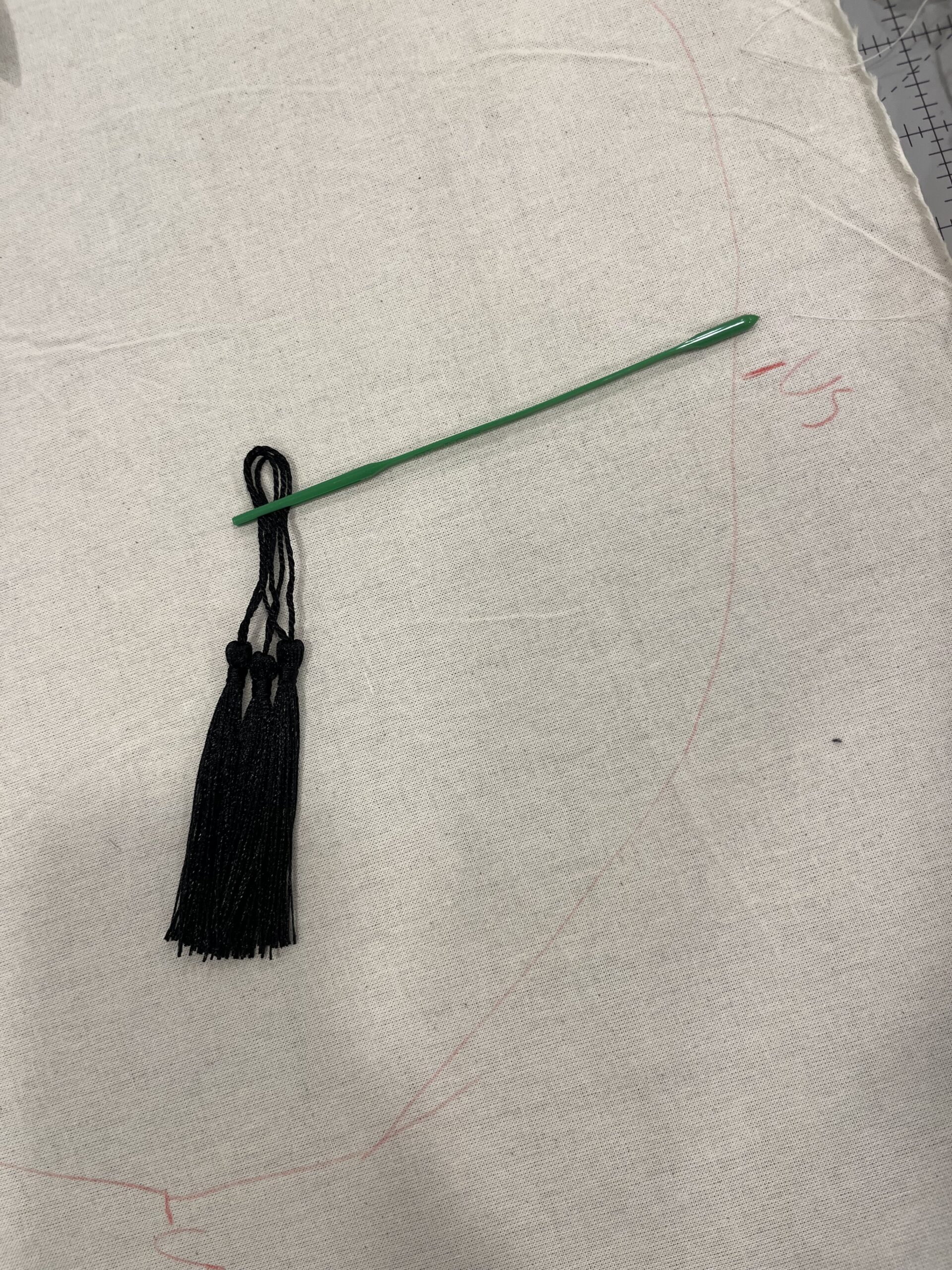 bundle of black tassels with their stems strung through the eye of a long green plastic needle