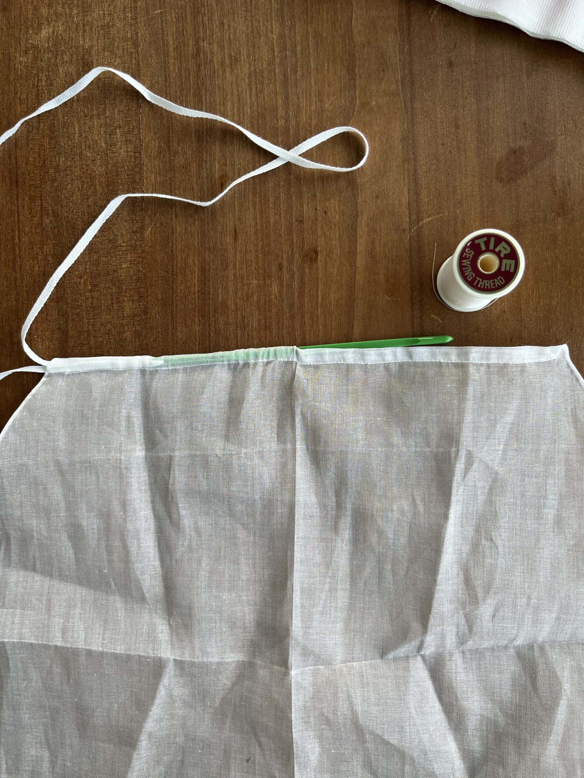 A long bodkin drawing a white tape through a channel sewn into white cotton fabric