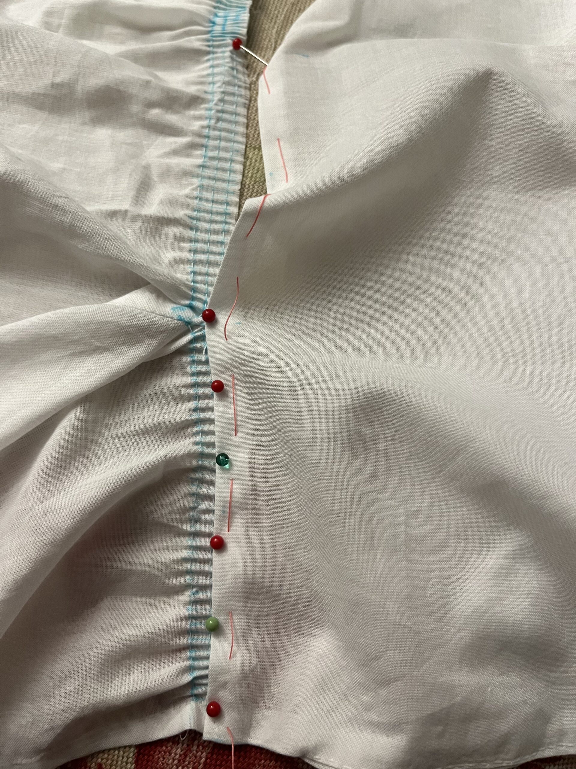 A row of stroked gathers being spread out and pinned along the neckline of a  white cotton 1790s chemisette
