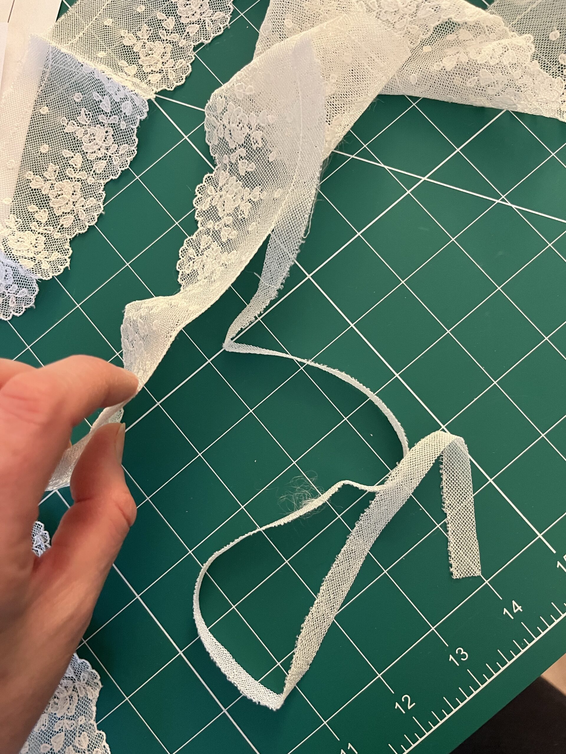 A hand holds a white piece of cotton lace - the bottom edge of the lace is being sliced away