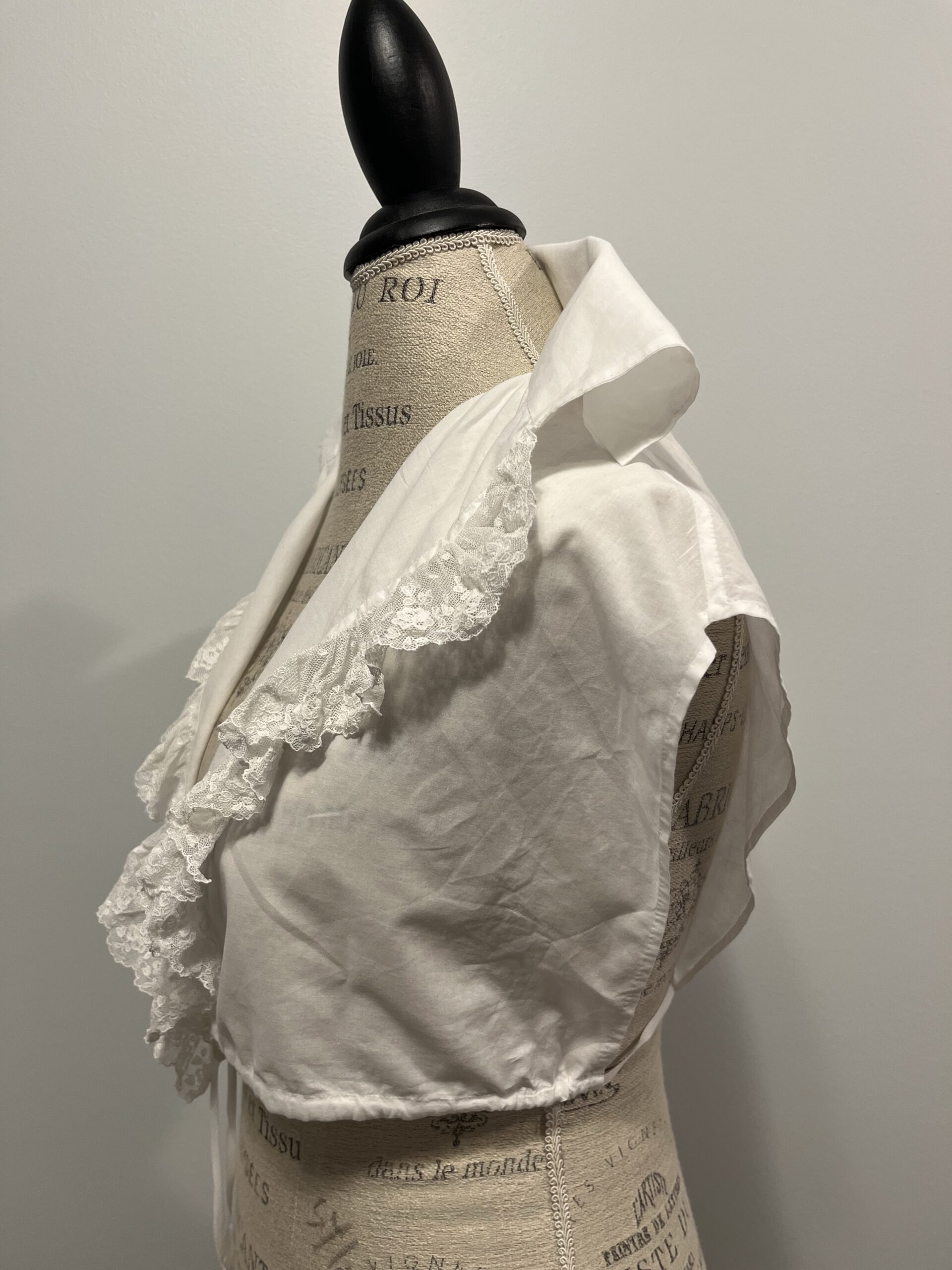 A 3/4 view of a white lace trimmed 1790s chemisette mounted on a mannequin