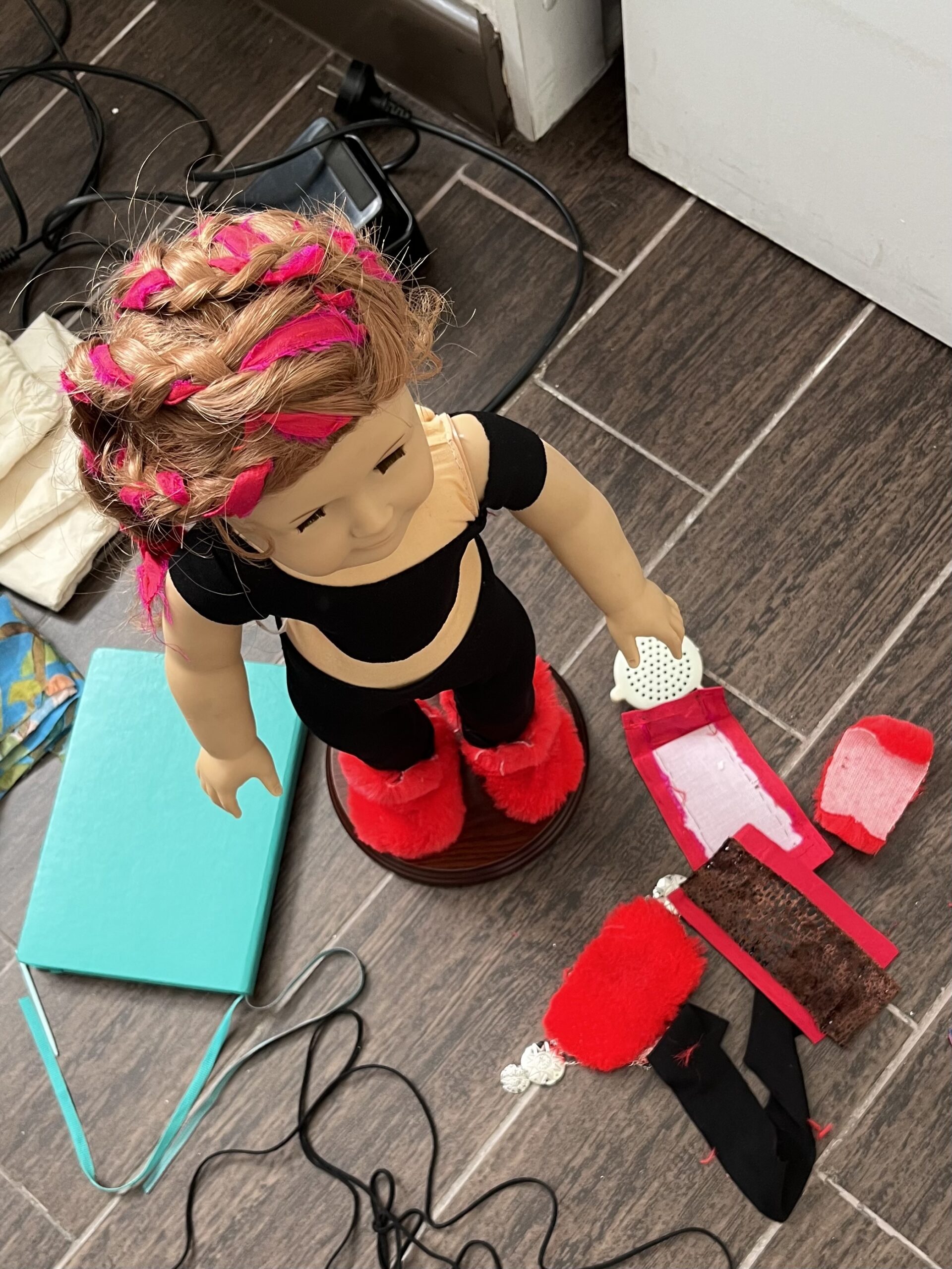 An American Girl Doll being dressed  in red fur and black jersey