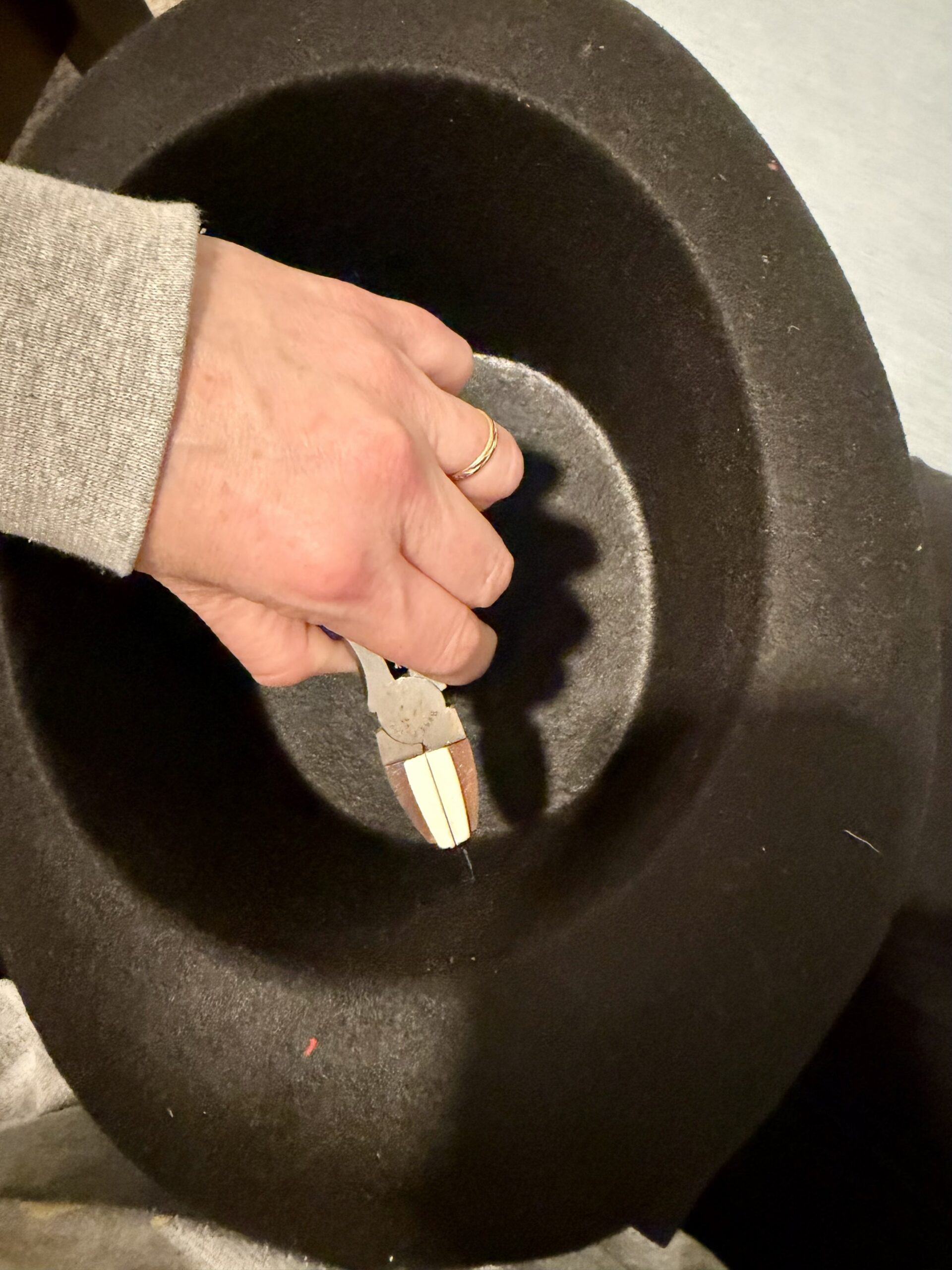 a hand reaches into a black hat. The hand holds a pair of pliers