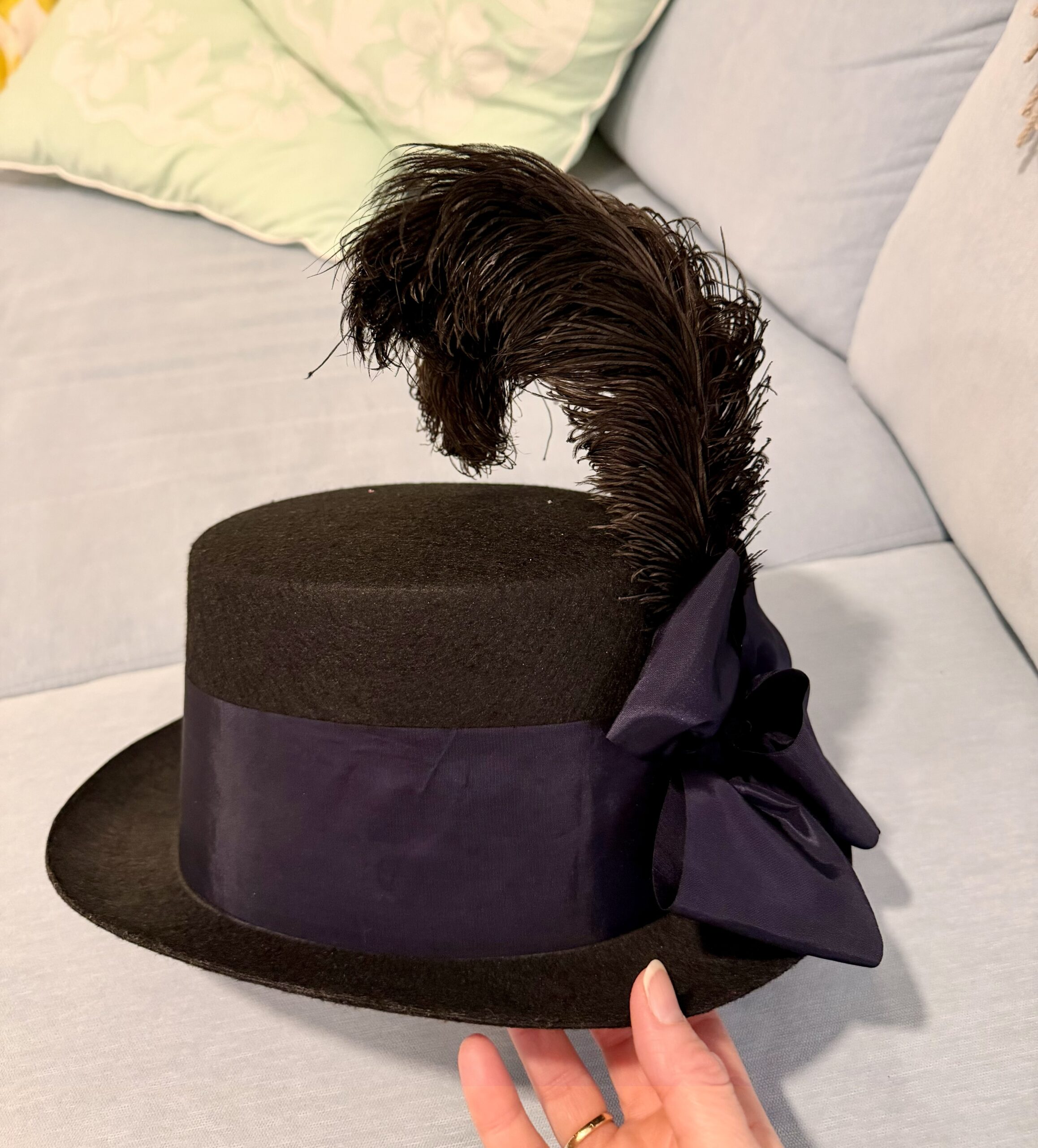 side view of a regency riding hat. it is decorated with a spray of feathers and a blue bow