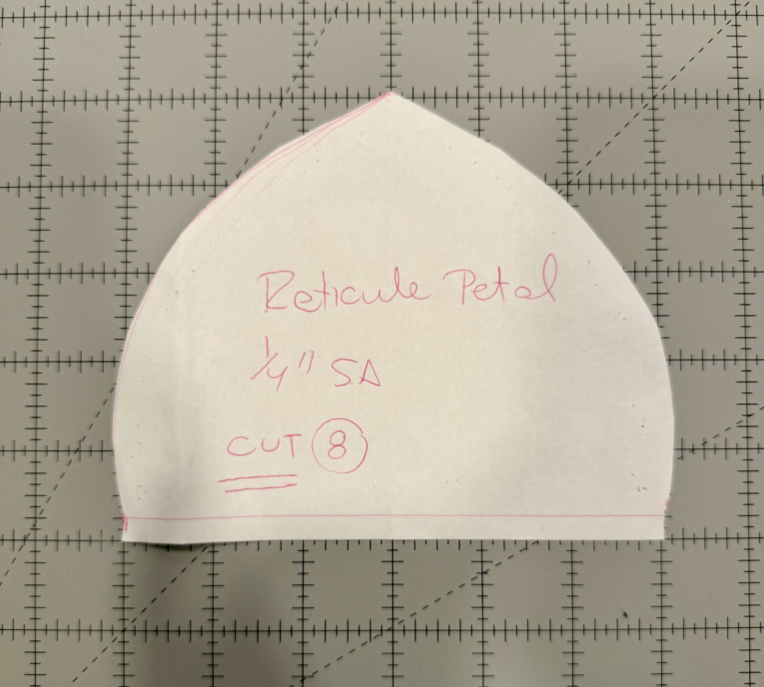 Paper pattern piece for the leaf of a raspberry regency reticule, laid on a grey cutting mat with 1-inch grid markings