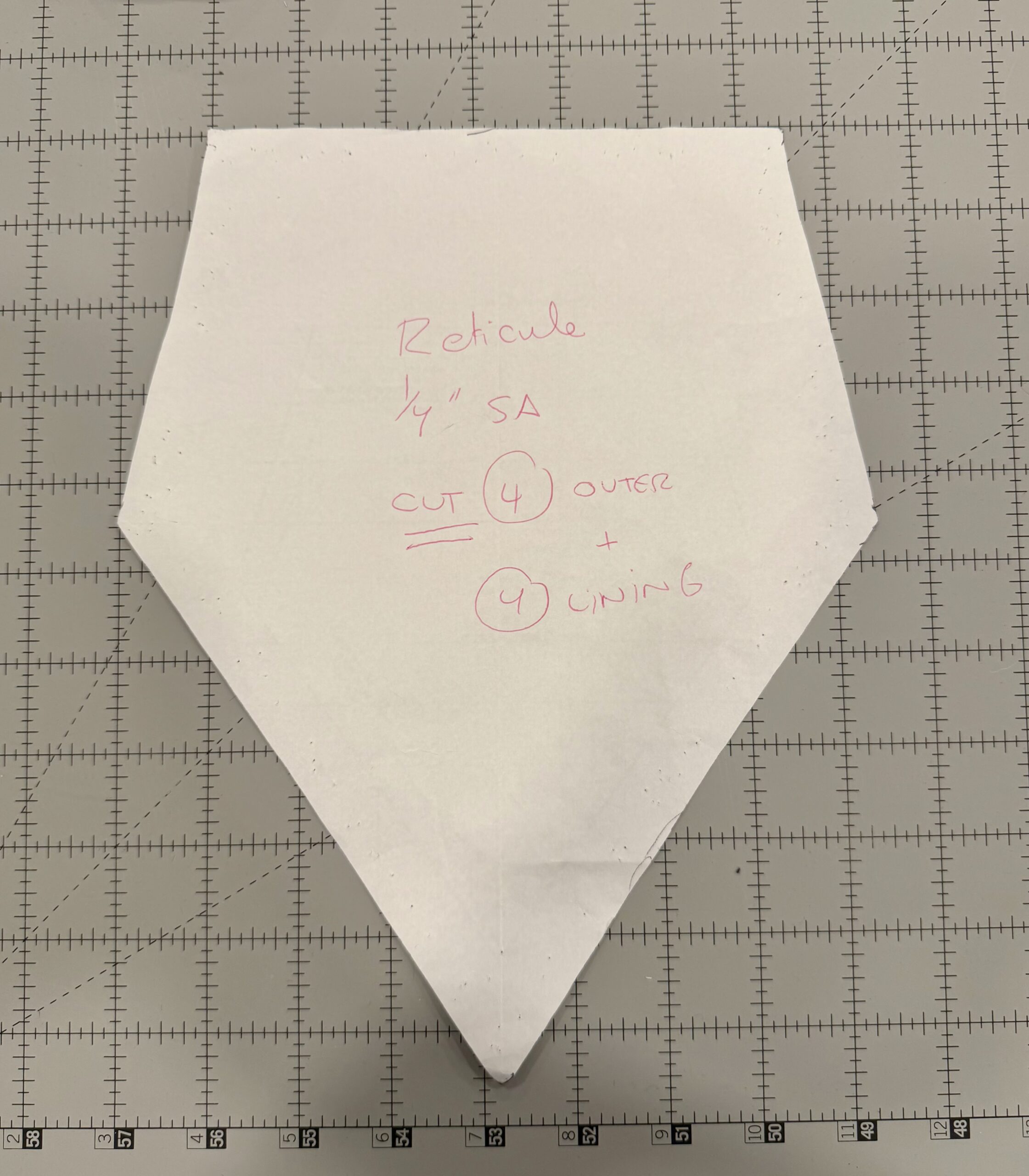 Paper pattern piece for the body of a raspberry regency reticule, laid on a grey cutting mat with 1-inch grid markings