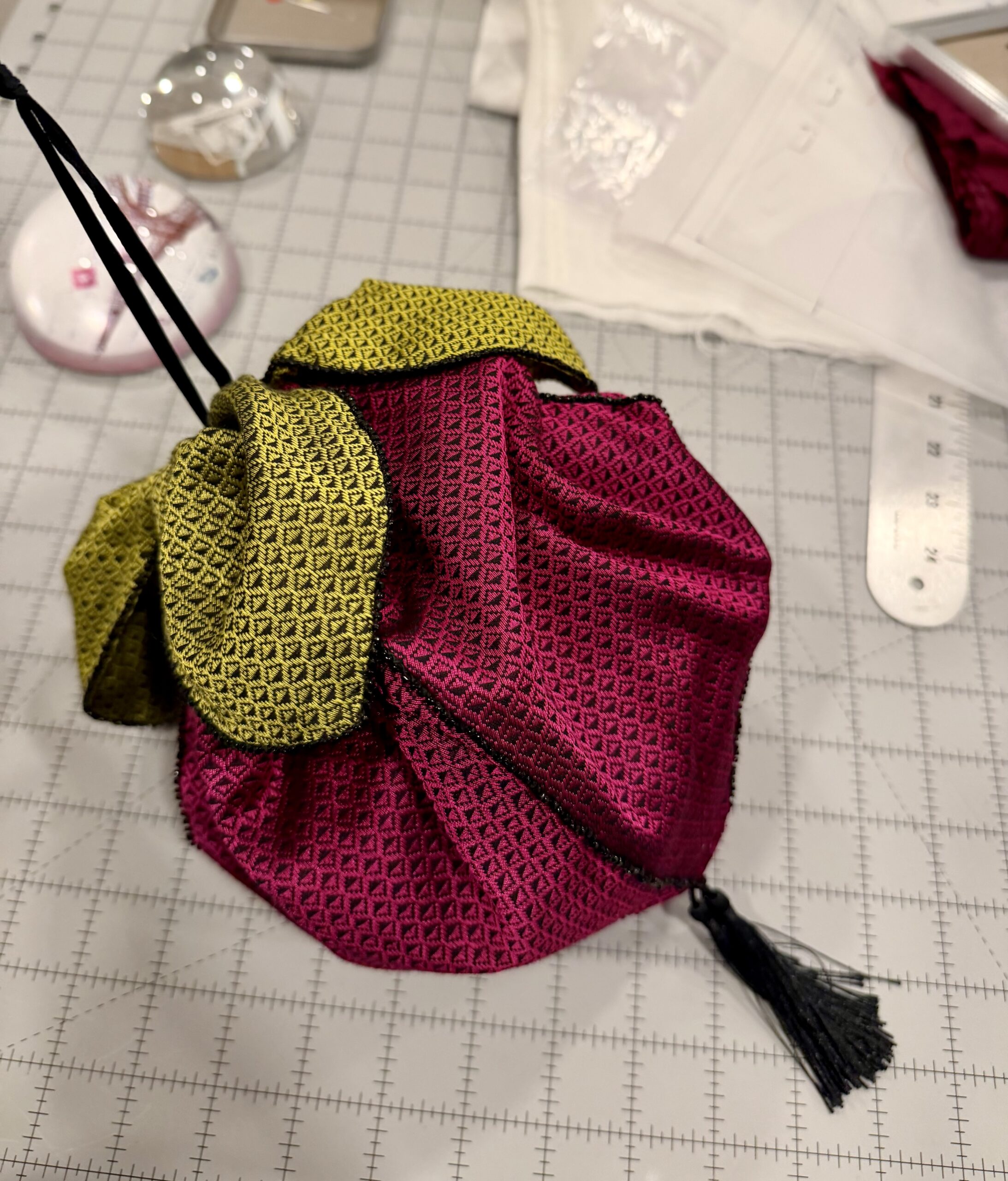 A raspberry regency reticule with green leaves and a tassel lies on a grey table