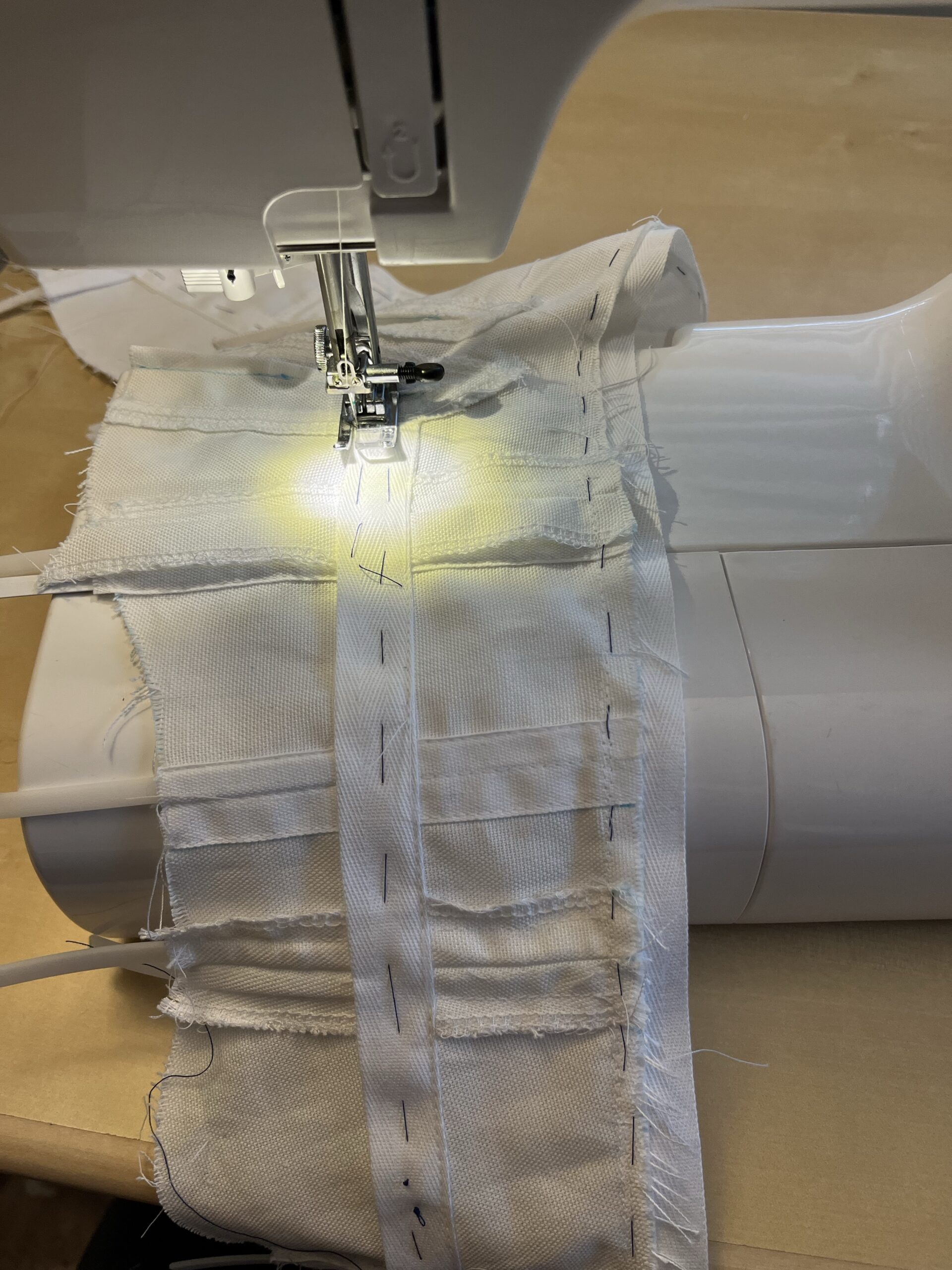 A pair of regency short stays sitting on a sewing machine - a long white tape is basted along the length of the stays