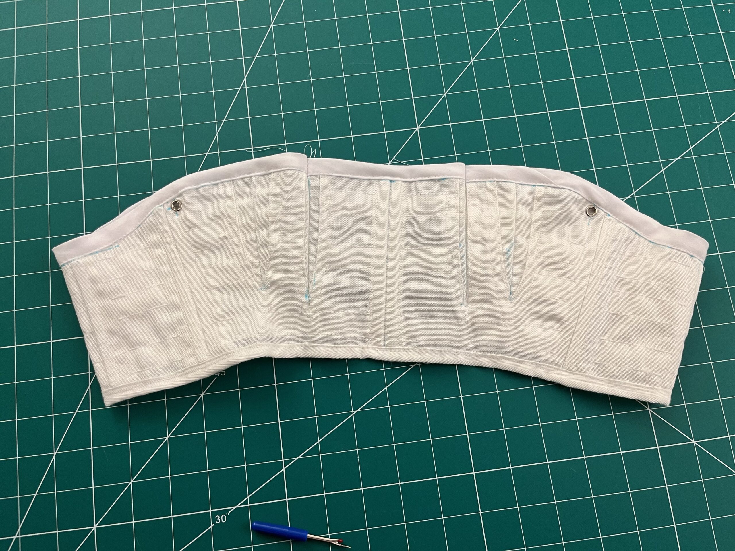 A pair of white regency short stays. Lots of horizontal stitching lines can be seen.