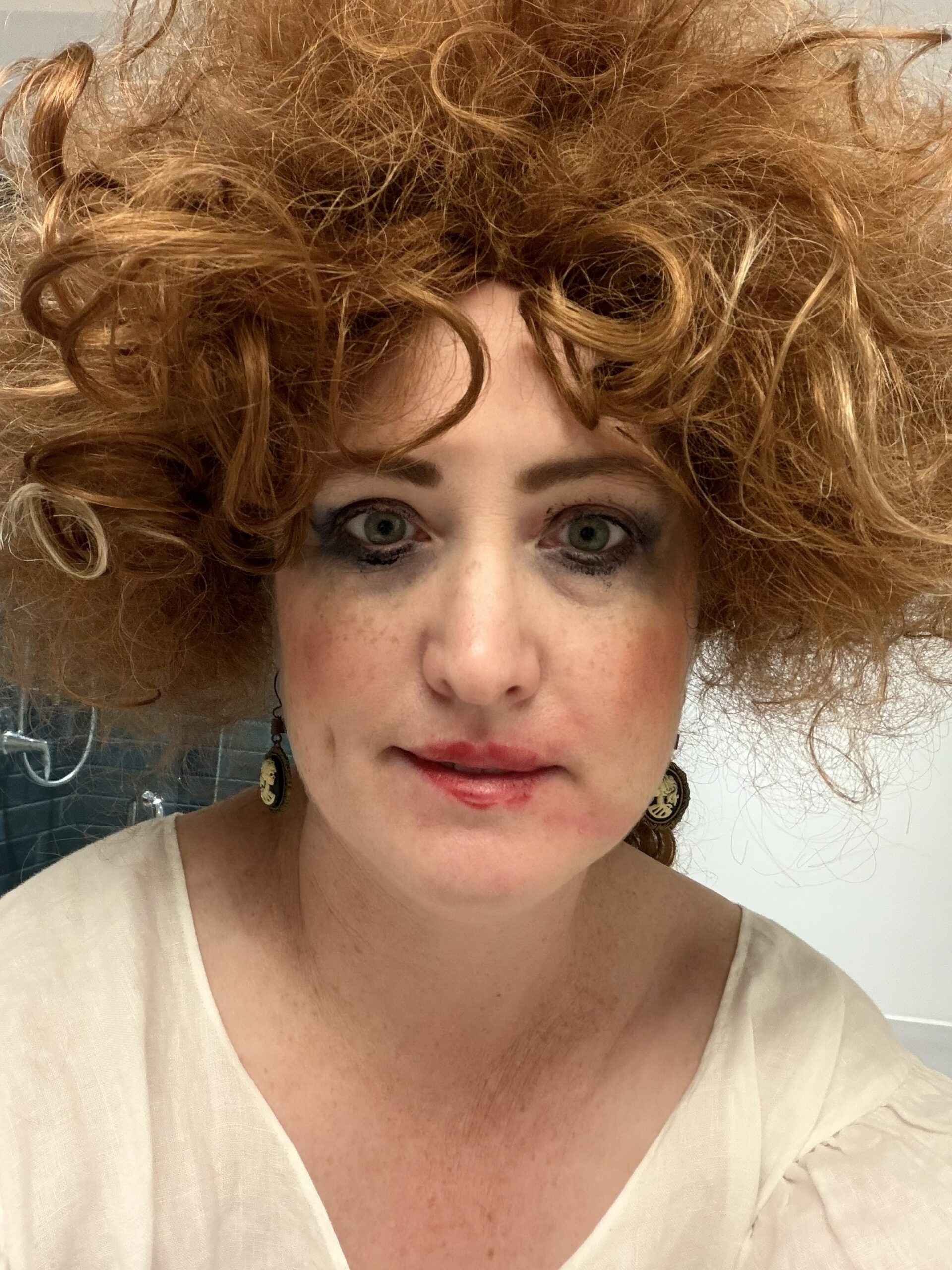 A close-up of a woman with smeared makeup and a ginger wig staring into the camera