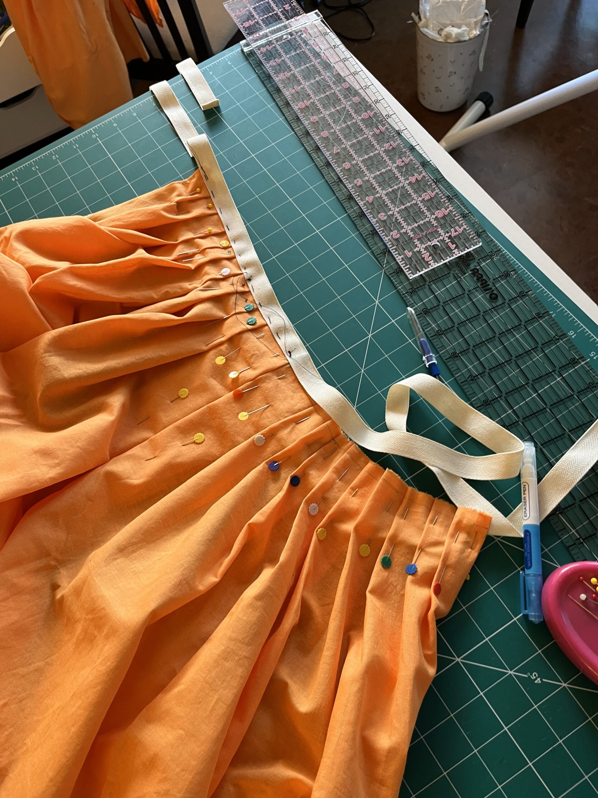 waist tape being basted to the waist of an orange 18th century petticoat
