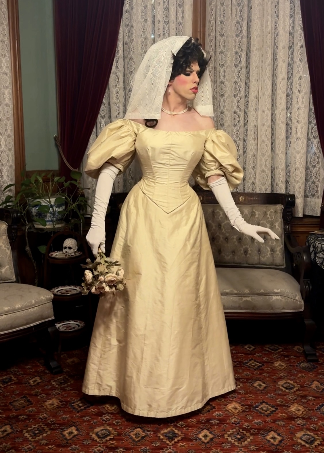 An elegant edwardian bride stands in facing the camera. She is wearing a white silk edwardian wedding dress and veil.