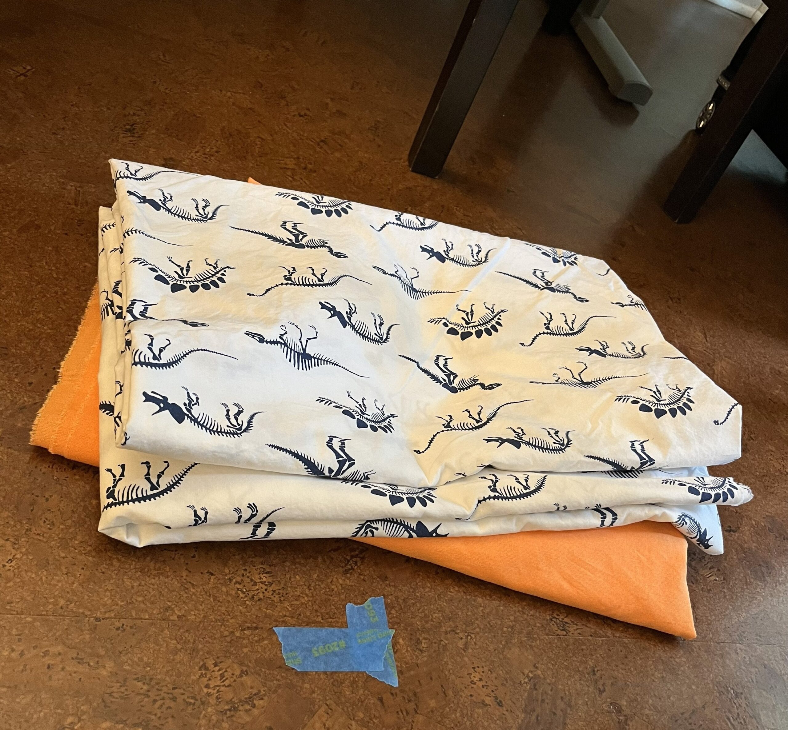 fabrics folded neatly on the floor - bright orange and white with dinosaur print