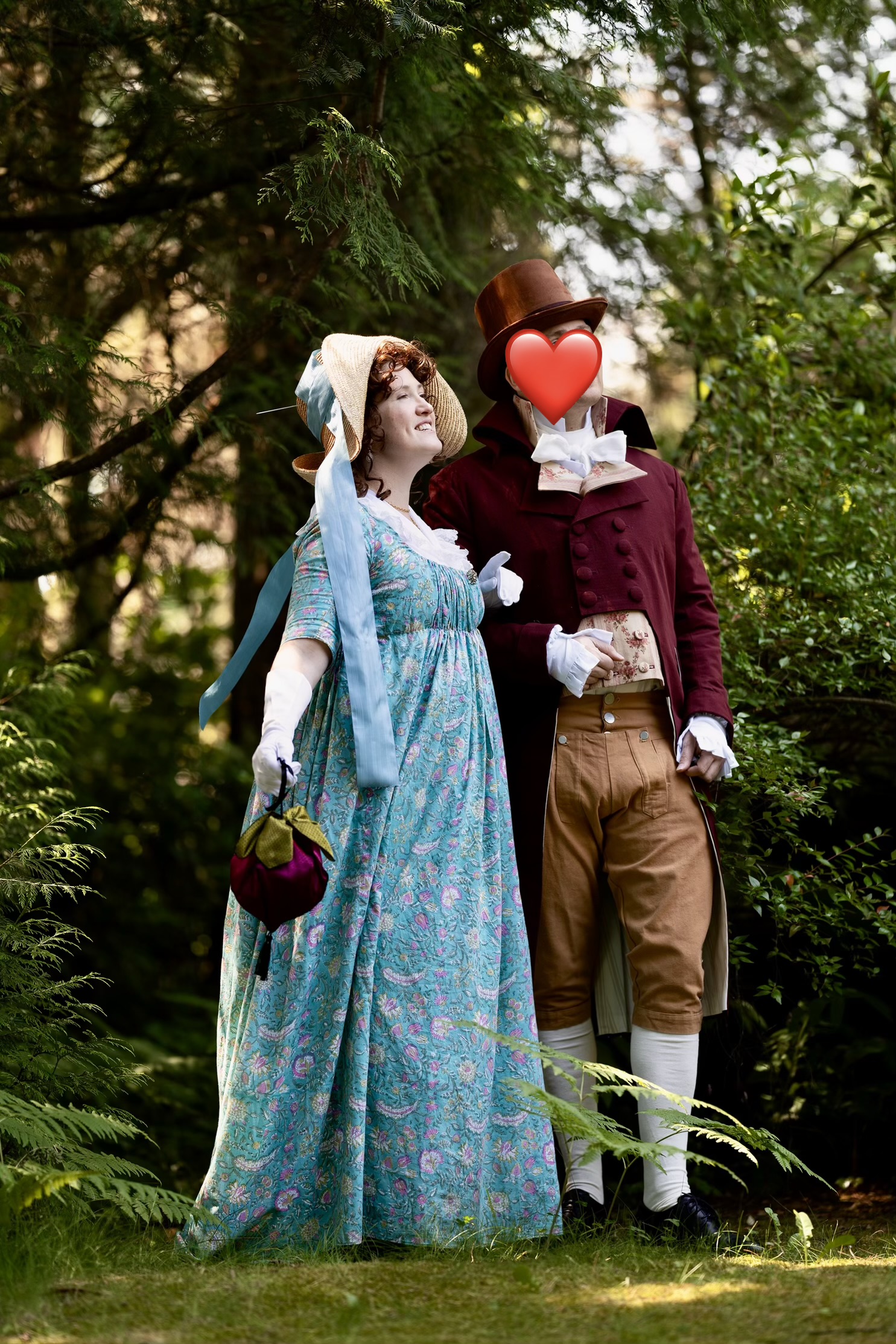 A man and a woman in regency clothing stand facing each other. Her face is obscured by a large straw hat. His face is obscured by a heart emoji