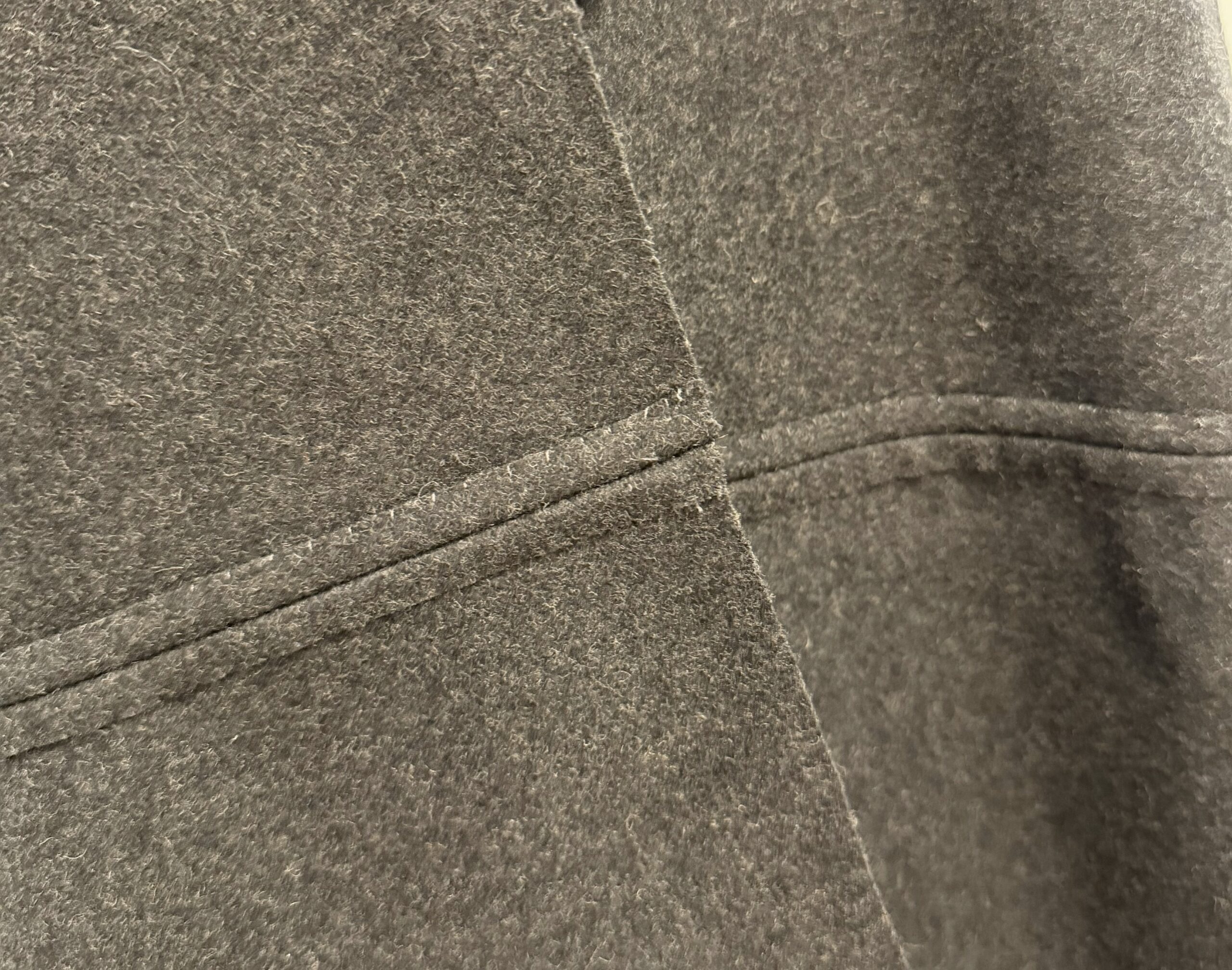 close-up of the inside of a sewn seam in grey wool felt - the seam allowances have been whipped down to the body of the garment