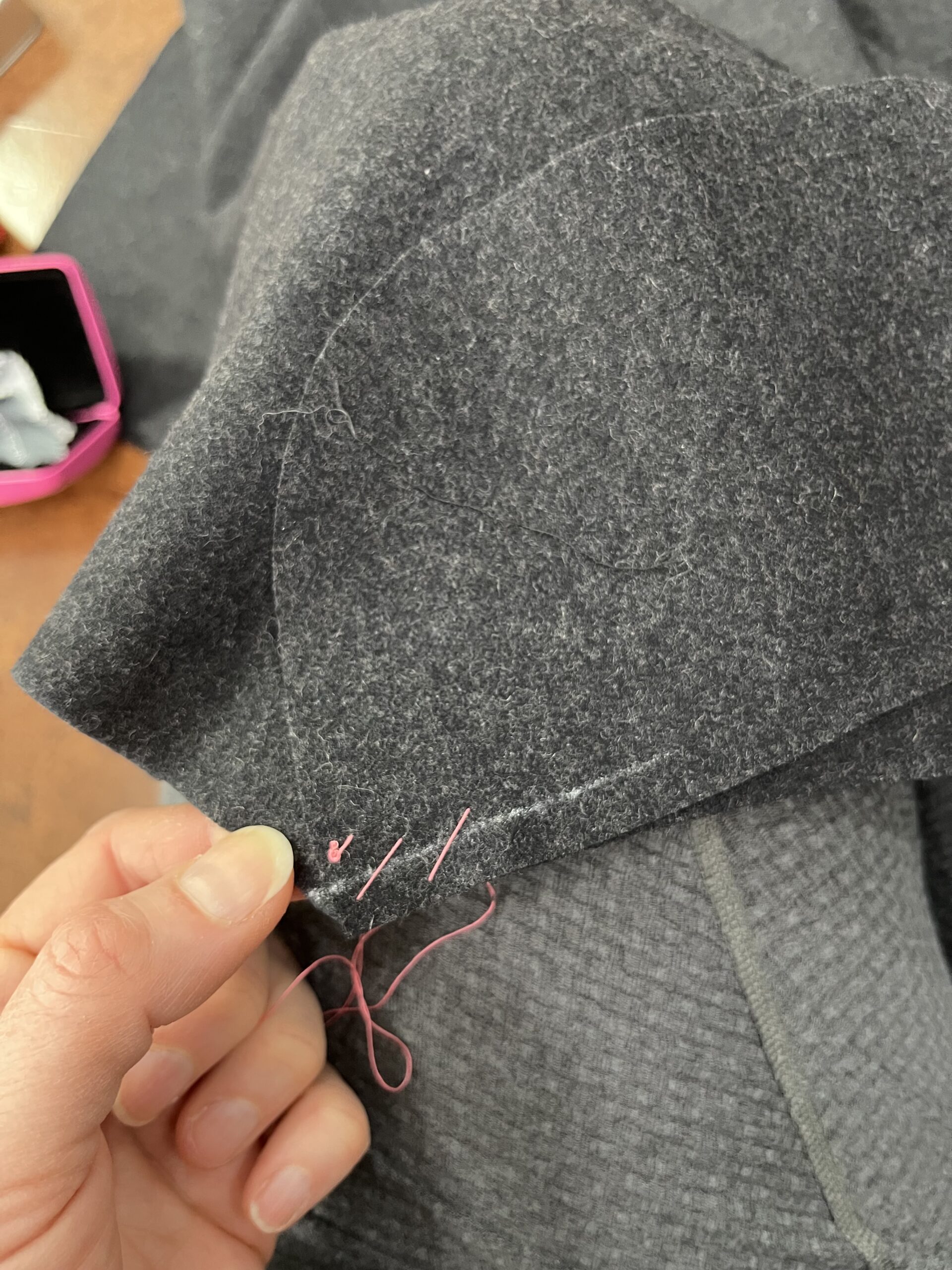 Pink basting stitches holding together layers of grey wool