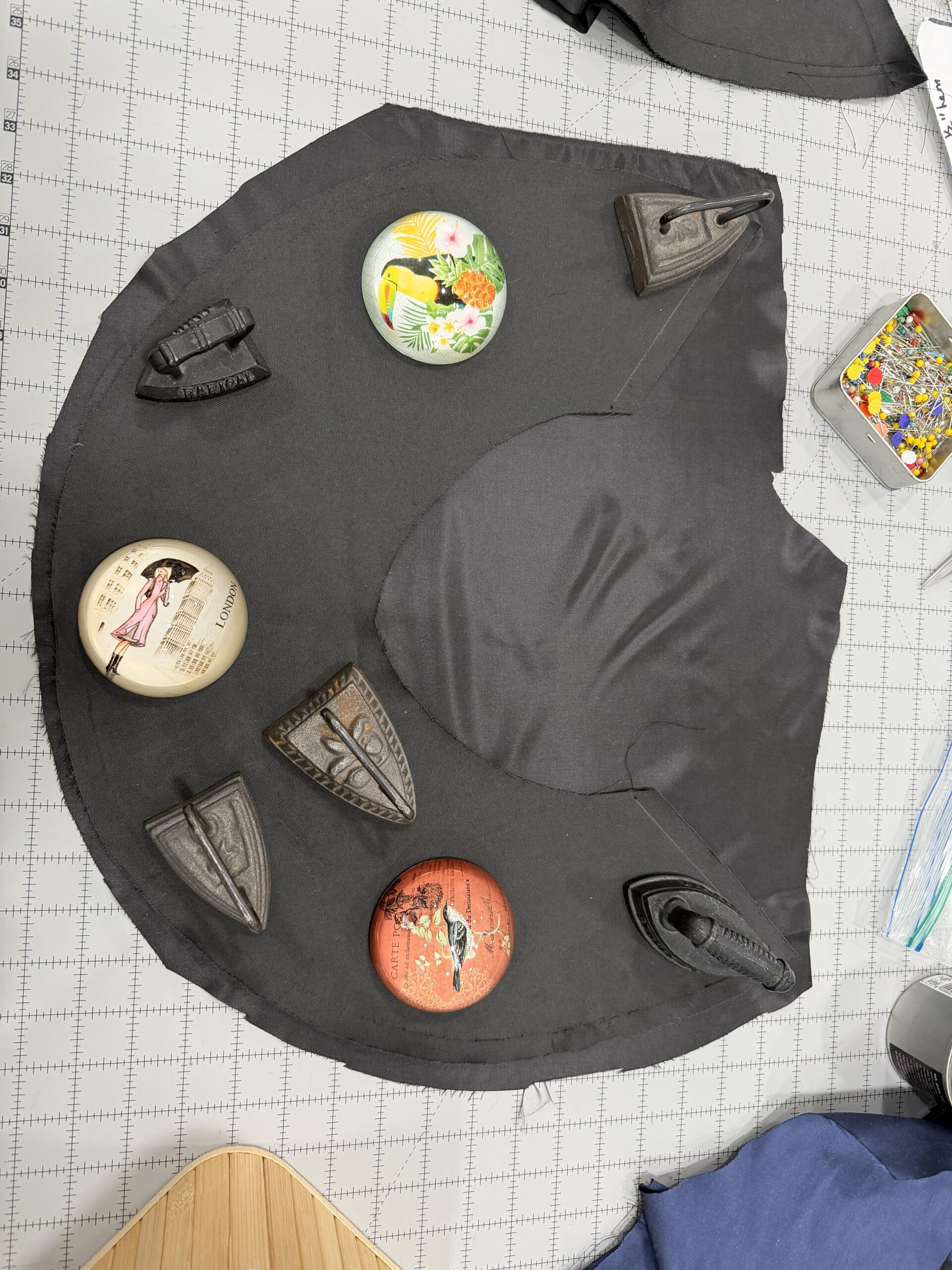 a crescent of black silk lying on a stretch of black velvet, held down by a LOT of  fabric weights