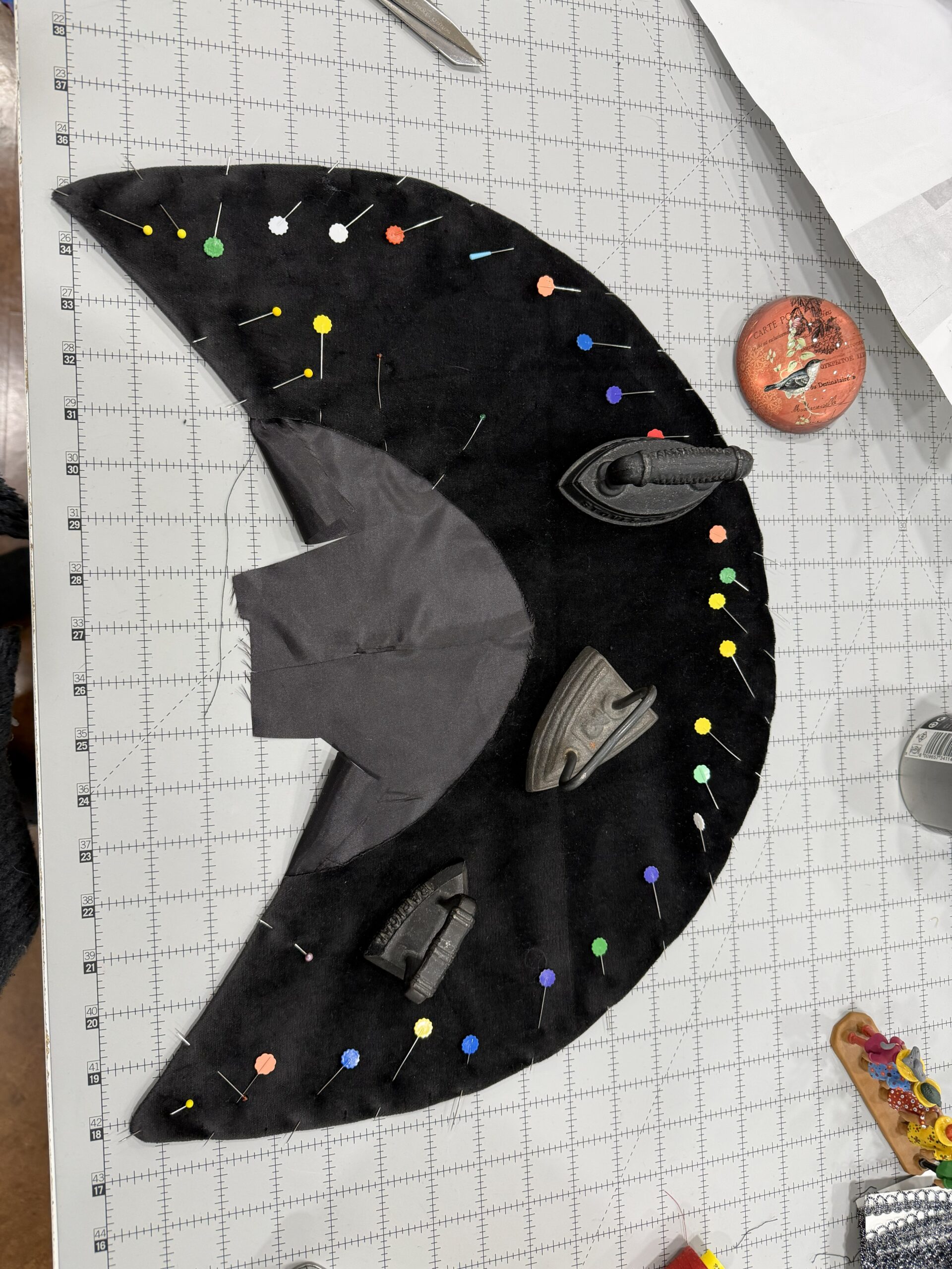 a crescent of black velvet being held down by a lot of pins and fabric weights