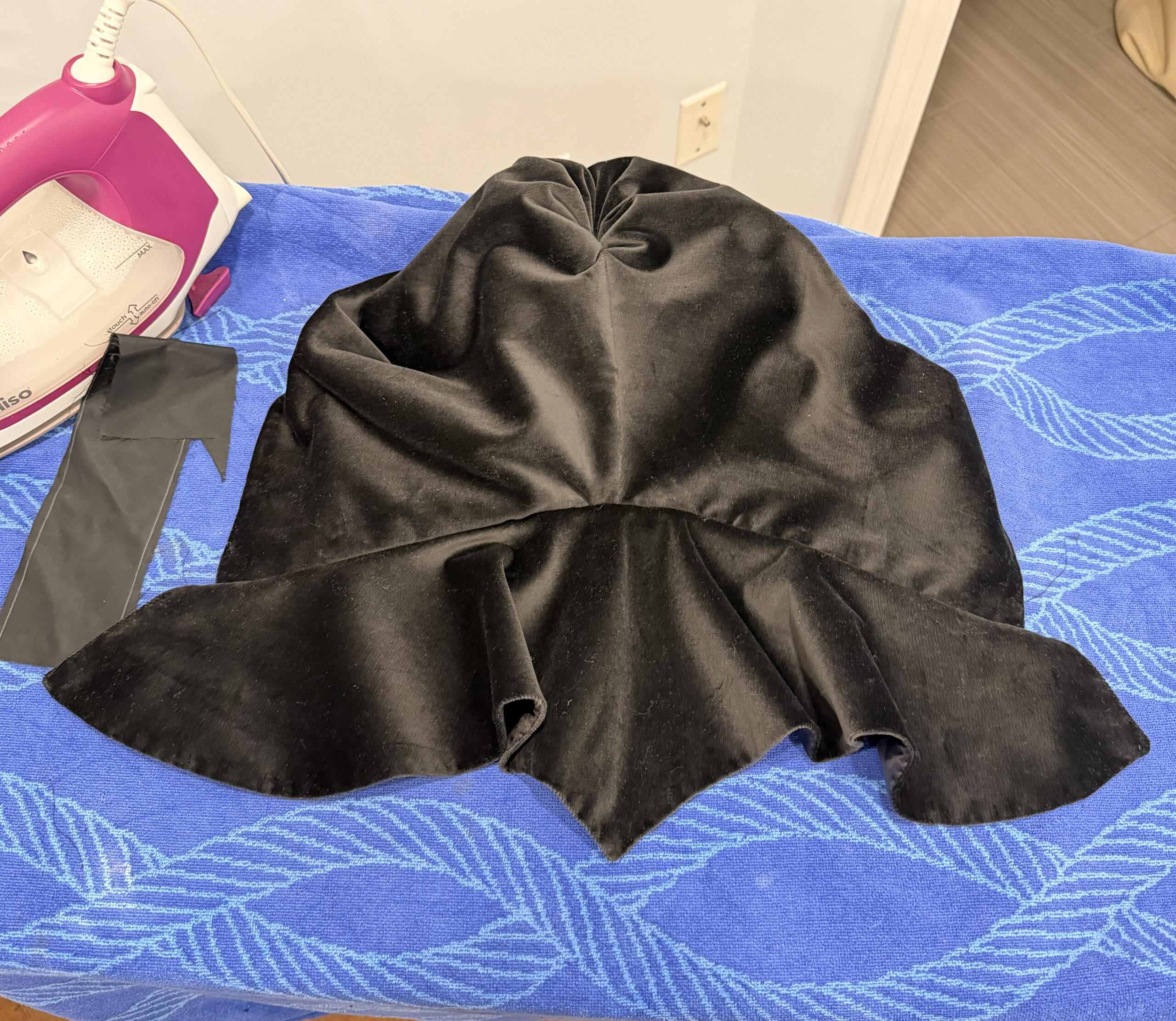 an 18th century black velvet hood, laid on its front on an ironing board