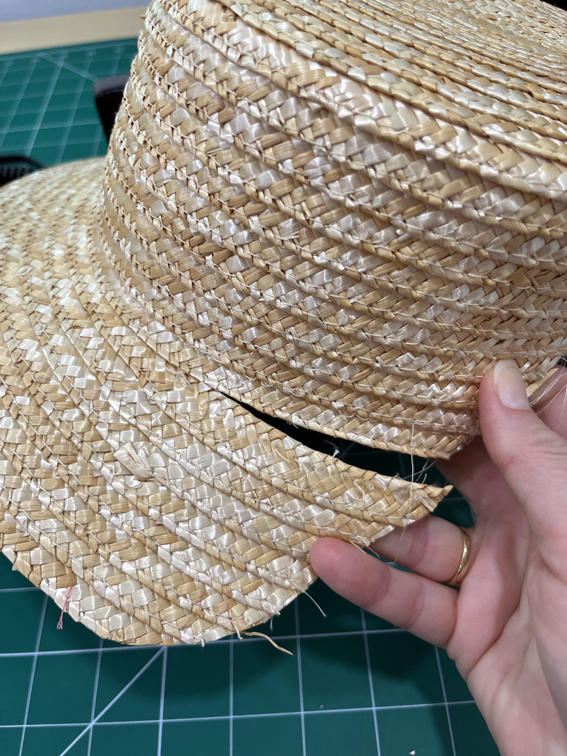 A hand holds a straw hat with the brim partially unpicked from the crown