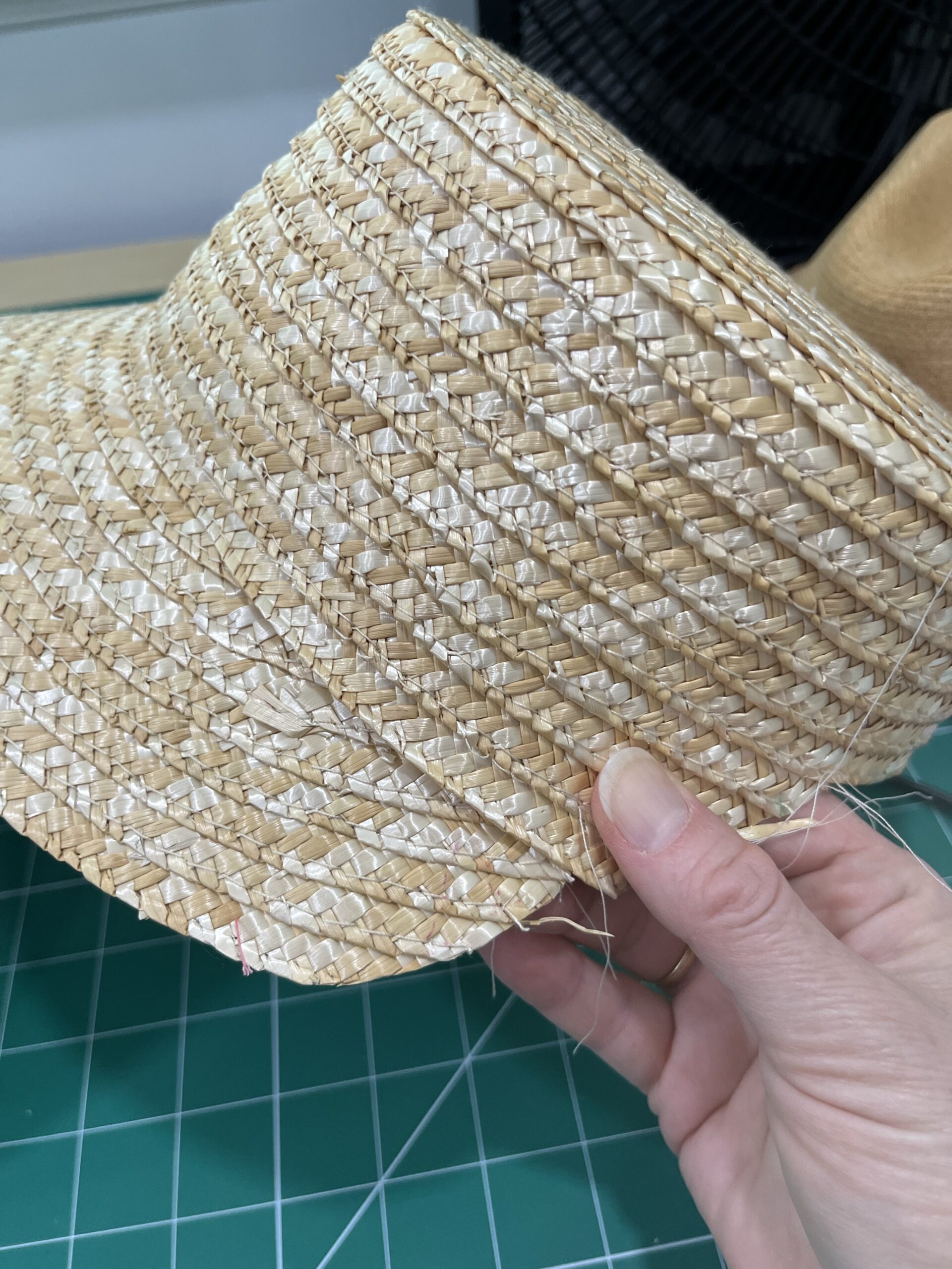 a hand holds a straw hat with part of the brim unpicked and folded under the crown