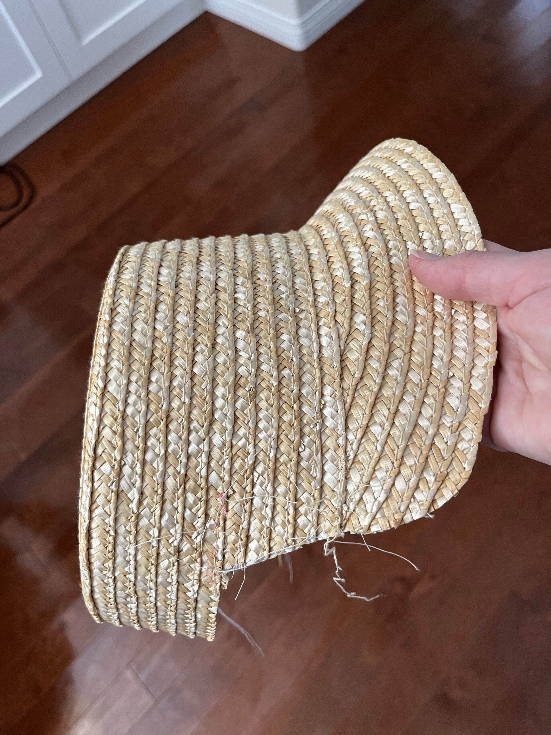 a hand holds a straw hat - a chunk has been cut out of the crown and part of the brim has been folded under the crown