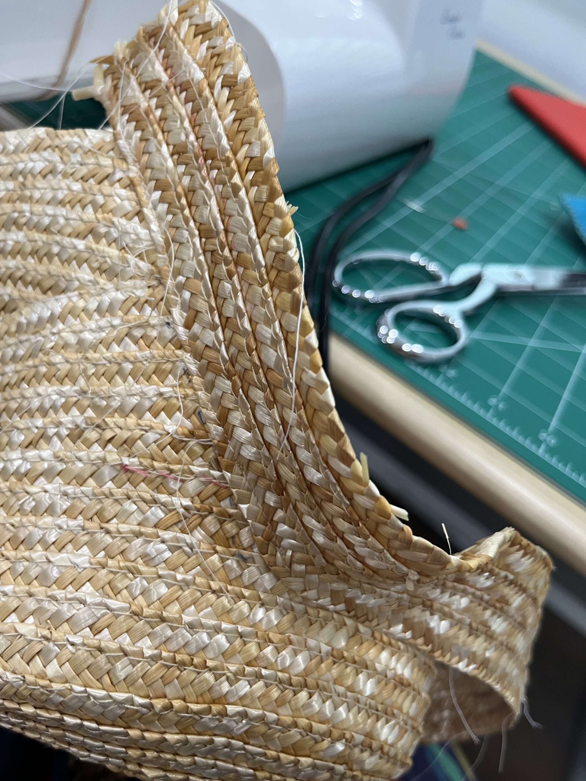 a wide band of straw being sewn onto a right-angle cut in the crown of a straw hat