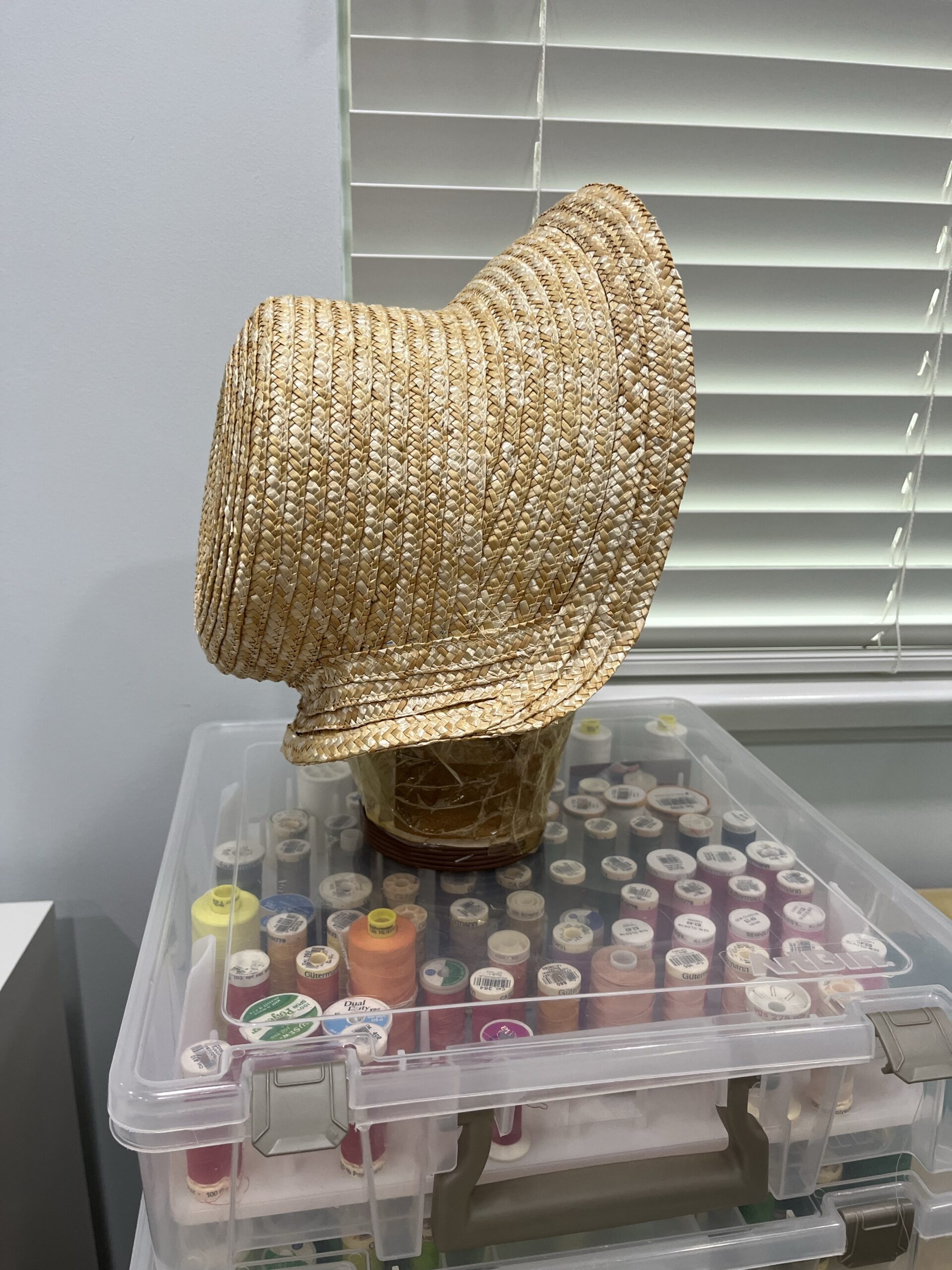An experimental straw bonnet c.1804-1809 sits on a box of multicolored threads