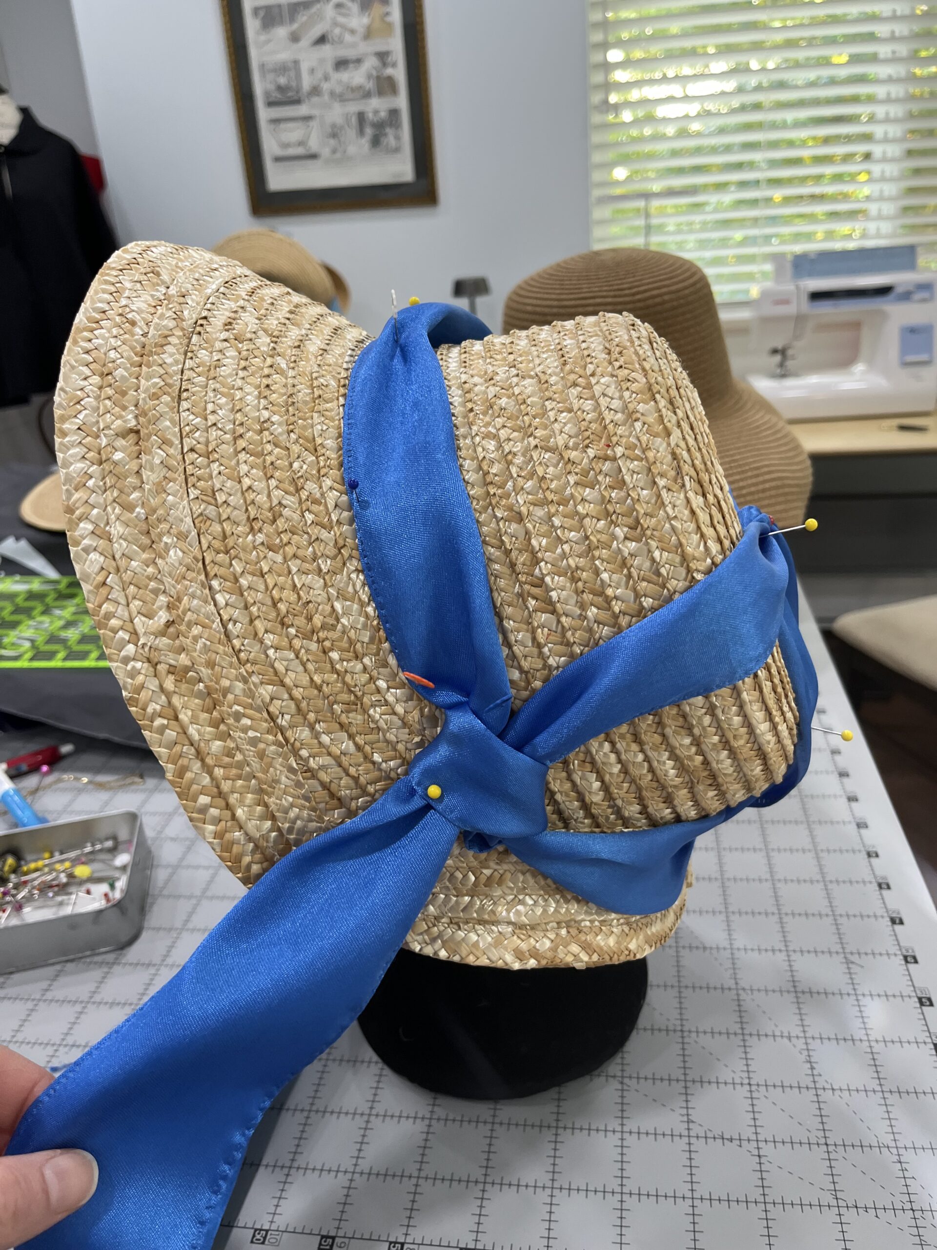 a straw bonnet with a blue ribbon twisted across and around and over the crown