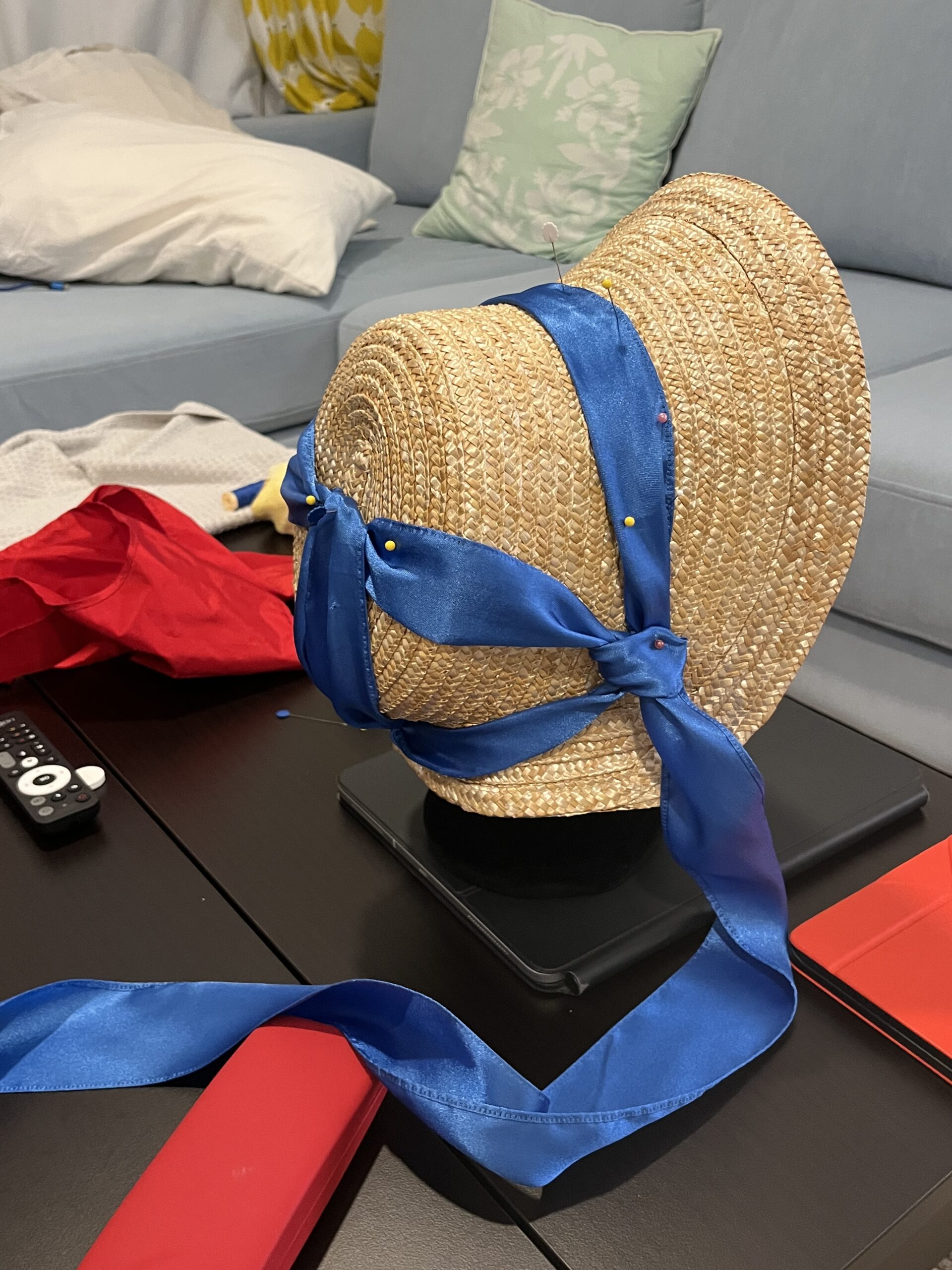 a straw bonnet with a blue ribbon twisted across and around and over the crown