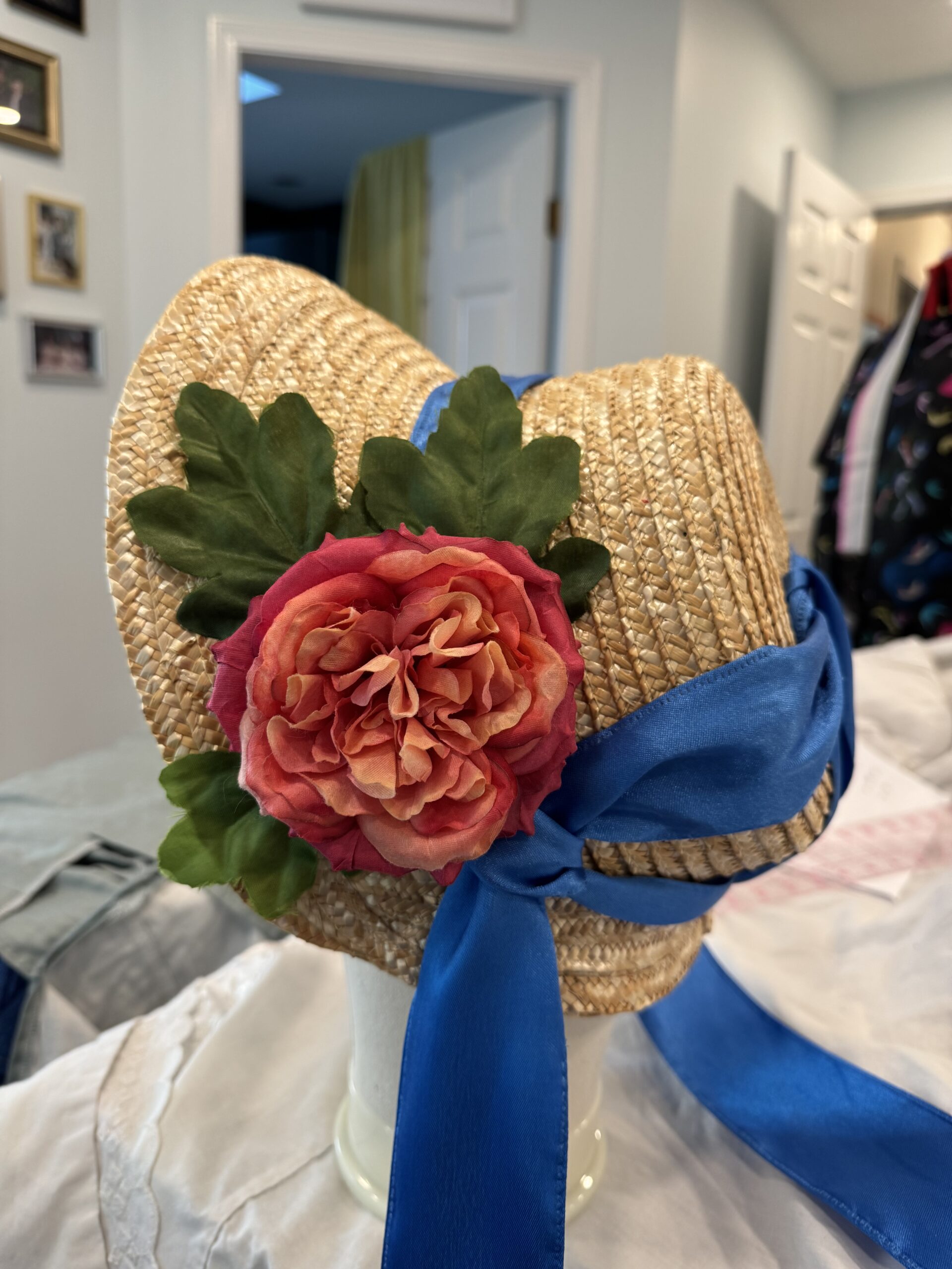 an experimental straw bonnet with a large red flower and green leaves attached to the left side
